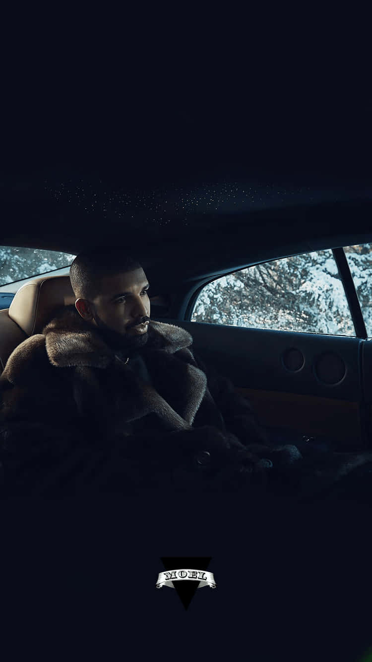 Aesthetic Drake 桌布 壁紙 — 一個穿著皮草大衣的男人晚上坐在車裡，透過車窗凝視著被雪覆蓋的樹木。