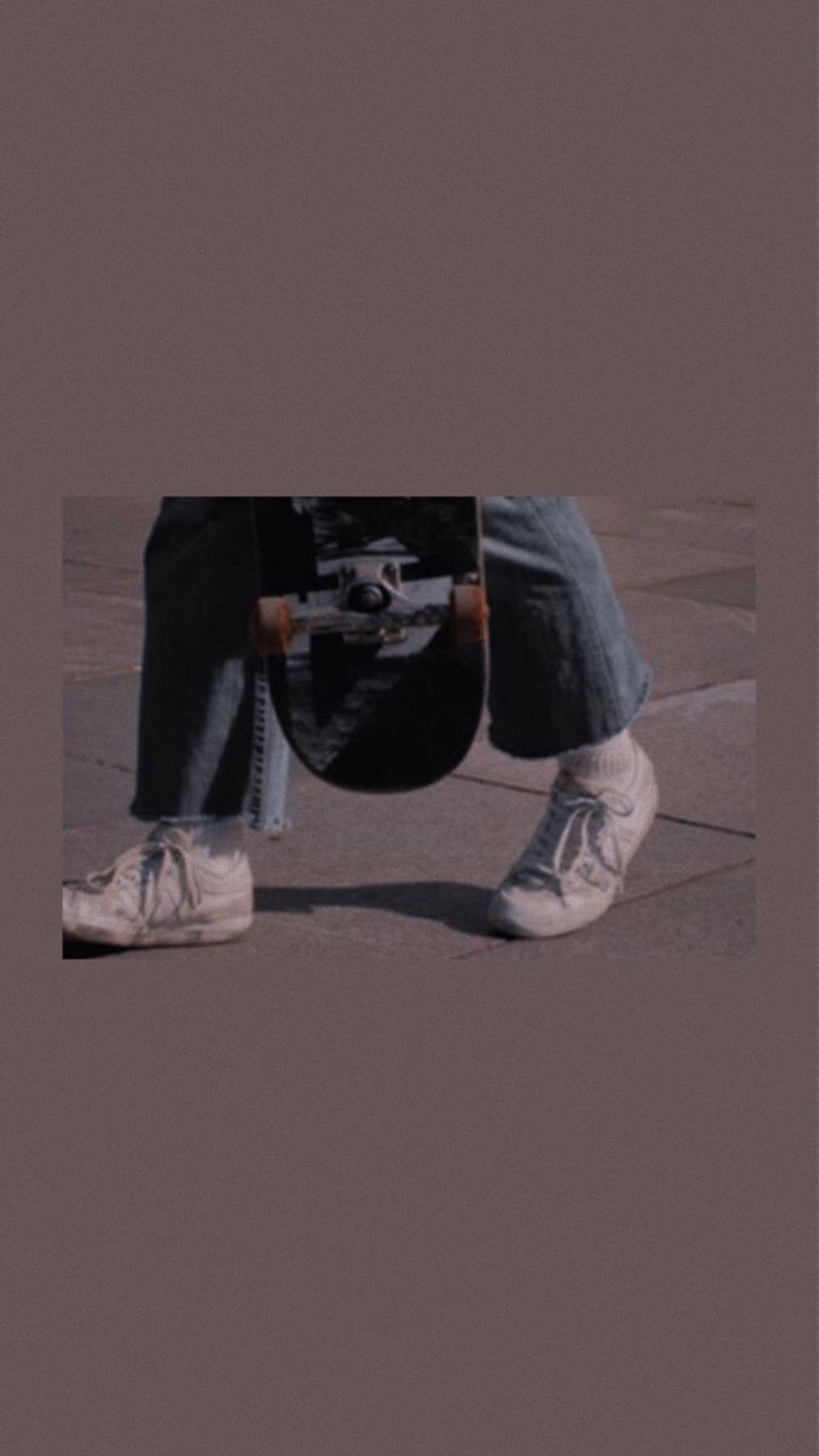 滑板 桌布 壁紙 — 一個穿著破洞牛仔褲和舊運動鞋的人，在鋪砌的人行道上將滑板夾在腋下。