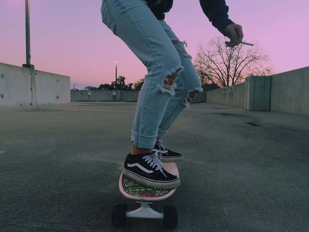 Retro Skateboard 桌布 壁紙 — 一個穿著破爛牛仔褲和黑色運動鞋的人，在黃昏時分粉紅色的天空下，在空蕩蕩的混凝土坡道上騎著粉紅色的滑板。