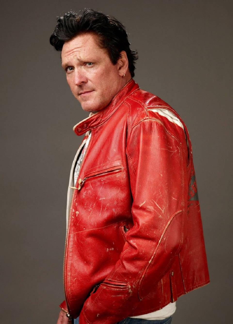 actor 桌布 壁紙 — 一個穿著破舊紅色皮夾克的男人，在純灰色背景下轉頭，表情嚴肅。
