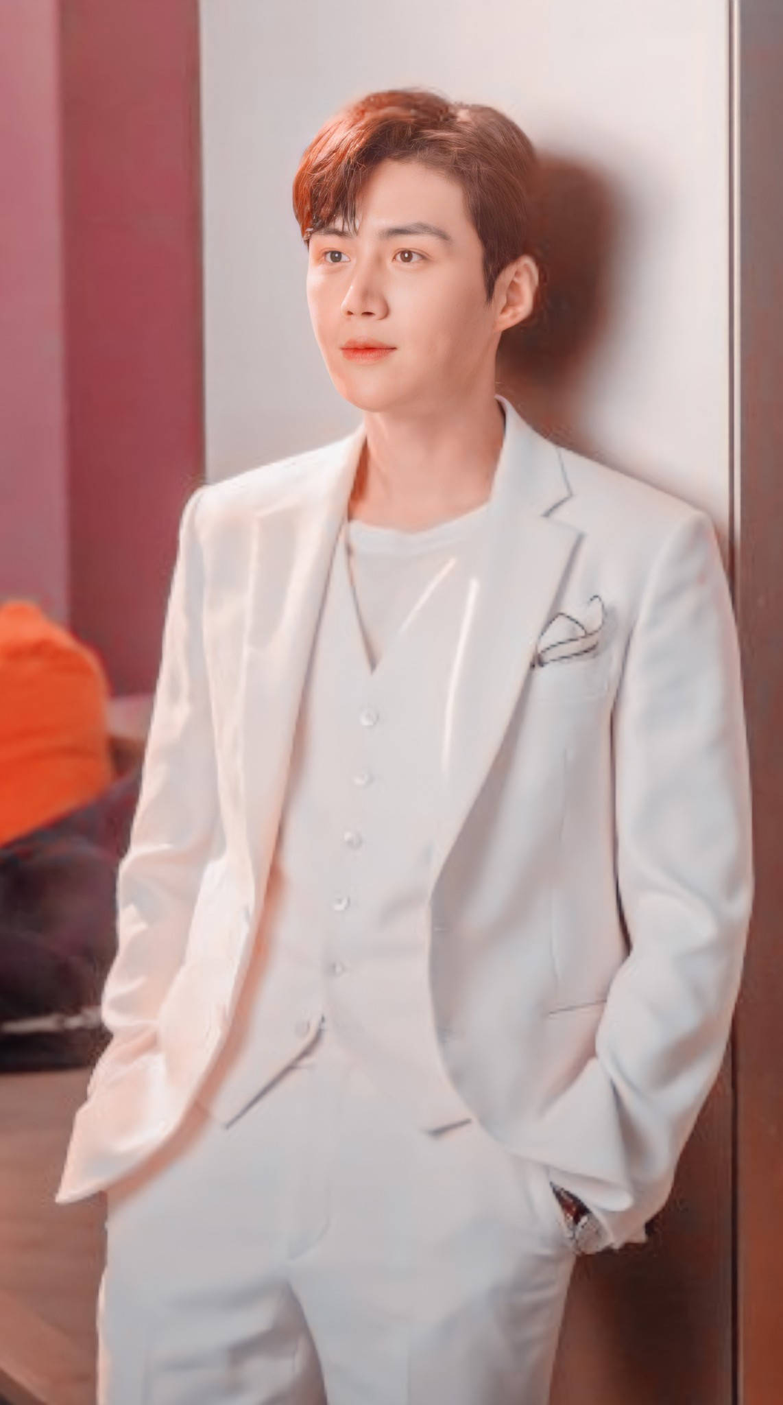 Kim Seon Ho 桌布 壁紙 — 一個穿著筆挺白色西裝的男人靠在牆上，背景是柔和的粉紅色和棕色調。