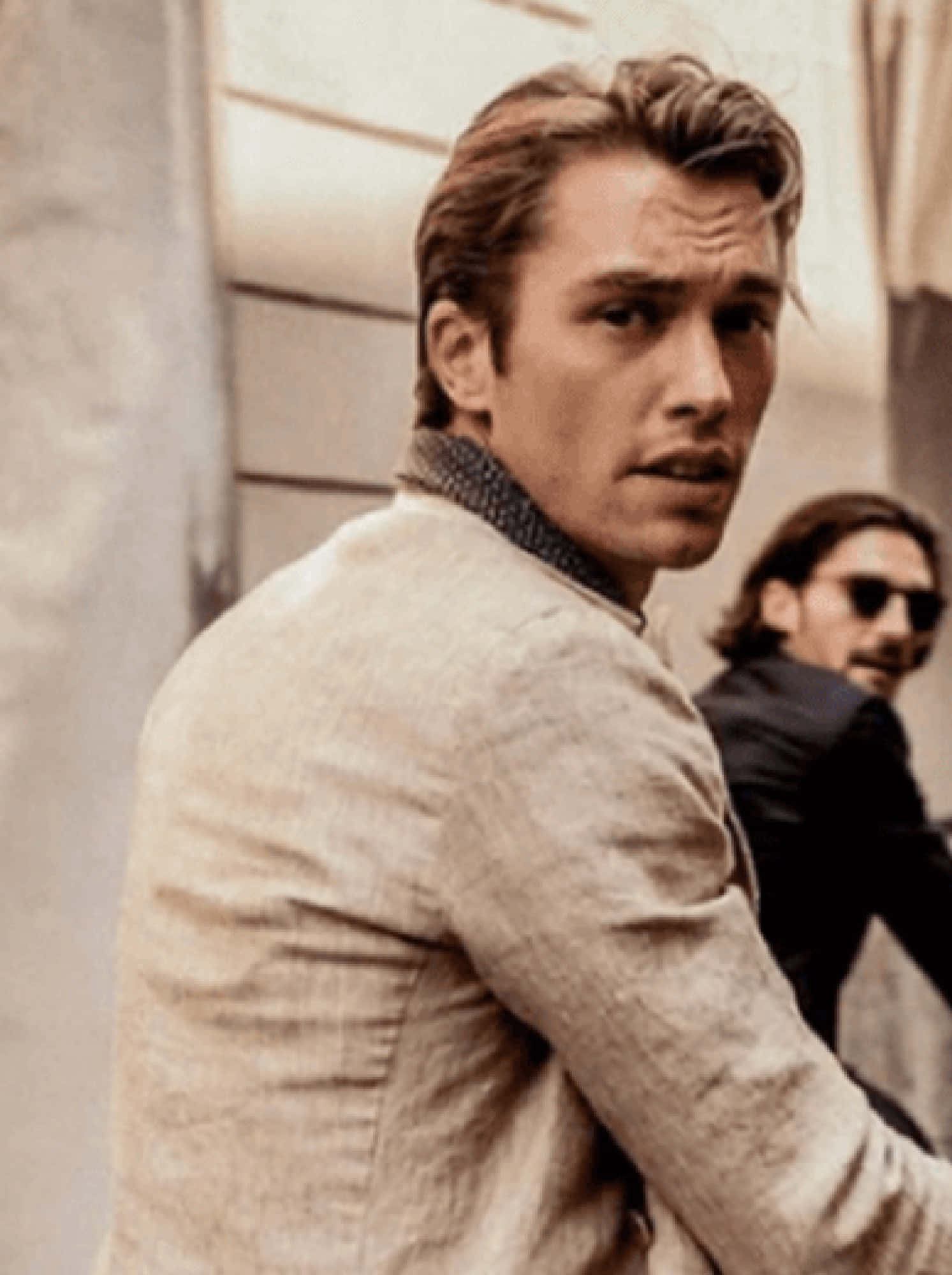 Handsome Man 桌布 壁紙 — 一個穿著米色亞麻外套的男人，在模糊的城市背景下，嚴肅地轉頭越過肩膀。