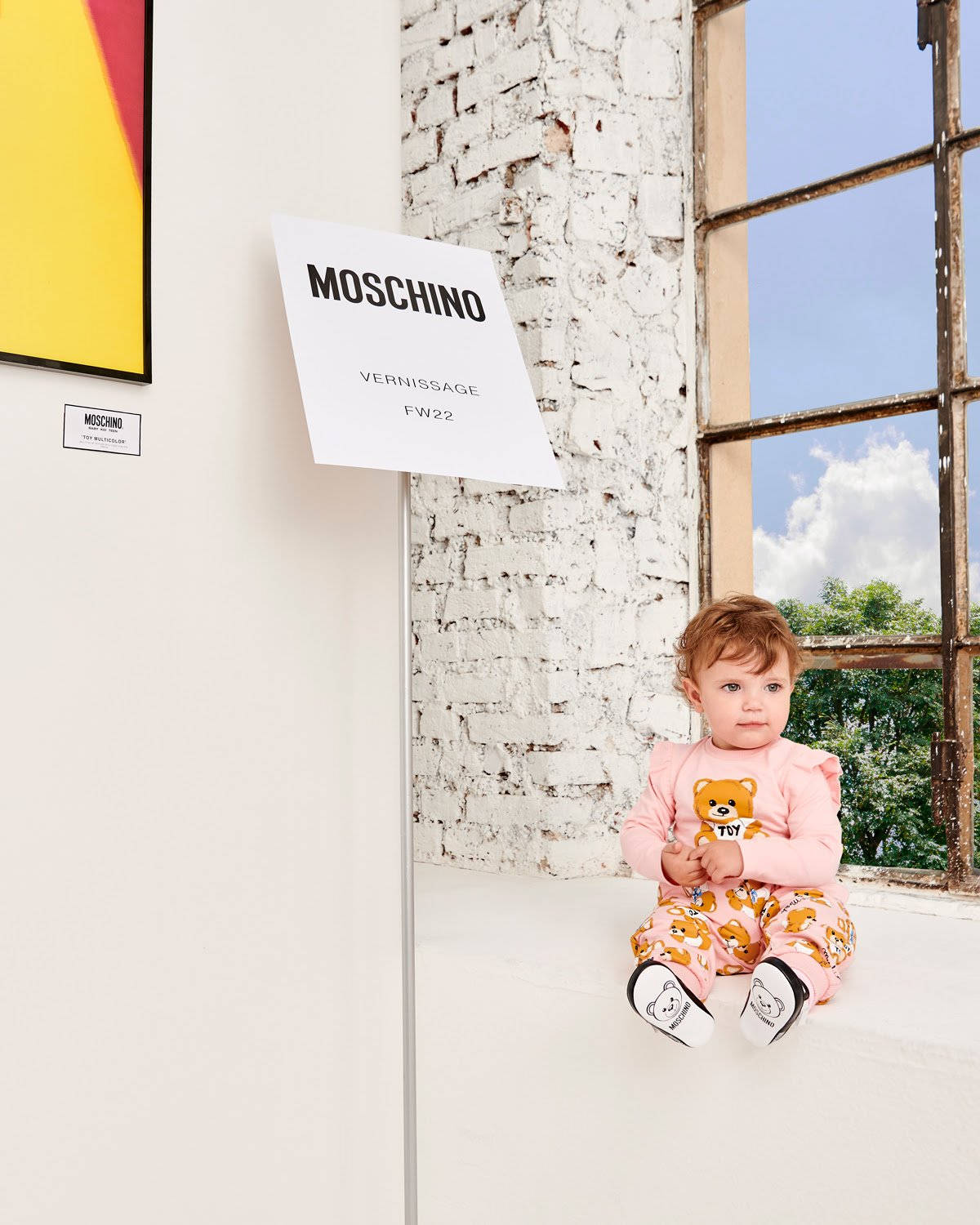 moschino 桌布 壁紙 — 一個穿著粉紅色小熊睡衣的嬰兒坐在白色窗台上，旁邊是一扇飽經風霜的窗戶，窗外是明亮的藍天。