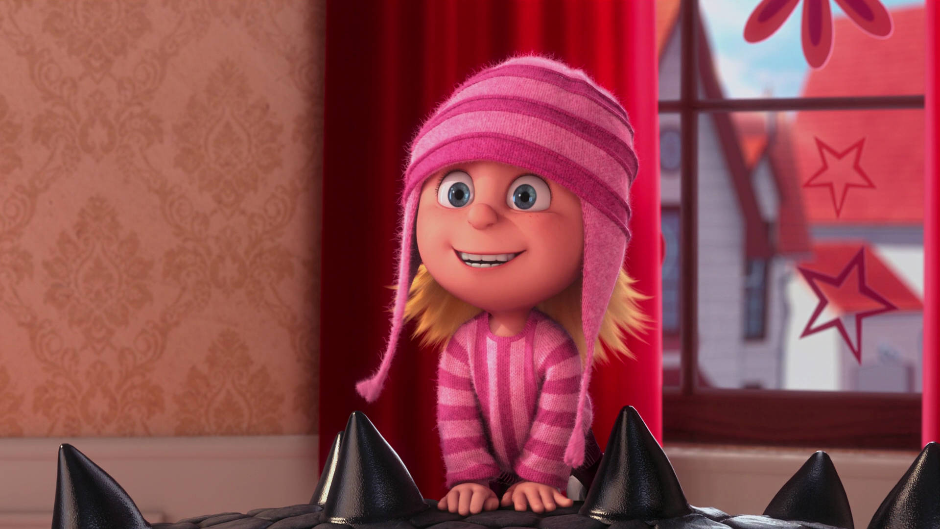 Despicable Me 2 桌布 壁紙 — 一個穿著粉紅色條紋睡衣和帽子的開朗動畫女孩，在靠近紅色窗簾的窗戶旁，從一個帶刺的黑色表面上方探出頭來。
