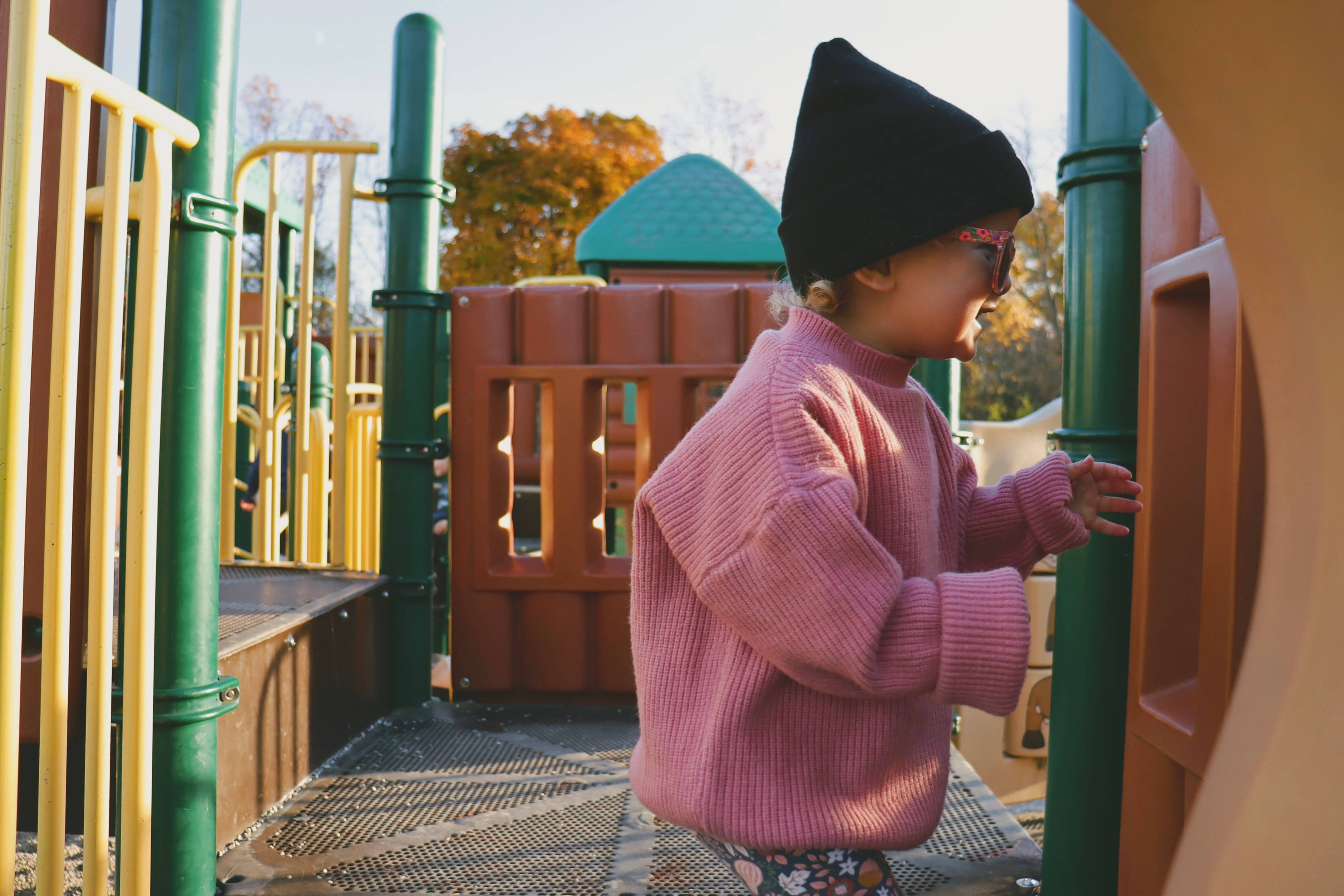Playground 桌布 壁紙 — 一個穿著粉紅色毛衣和黑色毛帽的小孩在晴朗的秋日探索色彩繽紛的遊樂場。