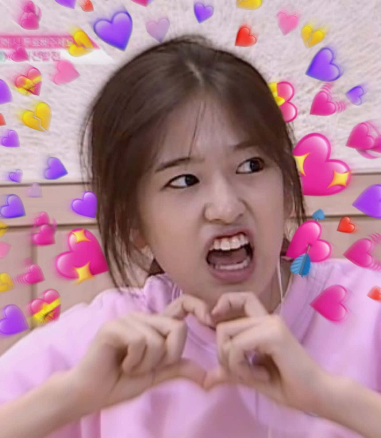 K-pop 桌布 壁紙 — 一個穿著粉紅色襯衫的小女孩，在漂浮的彩色心形表情符號環繞下，用雙手做出心形手勢。