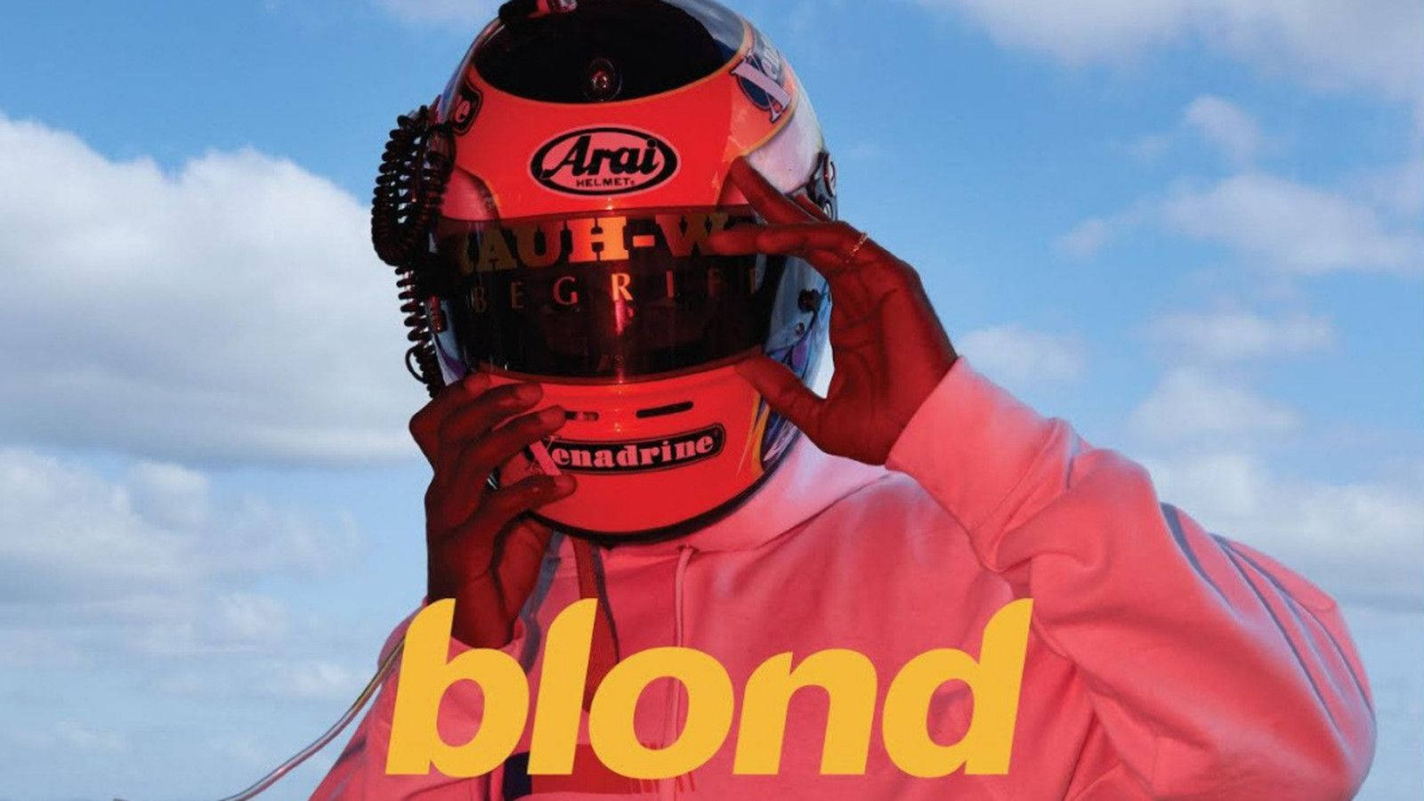 Frank Ocean 桌布 壁紙 — 一個穿著粉紅色連帽衫的人正在明亮的藍天白雲下調整紅色賽車頭盔。