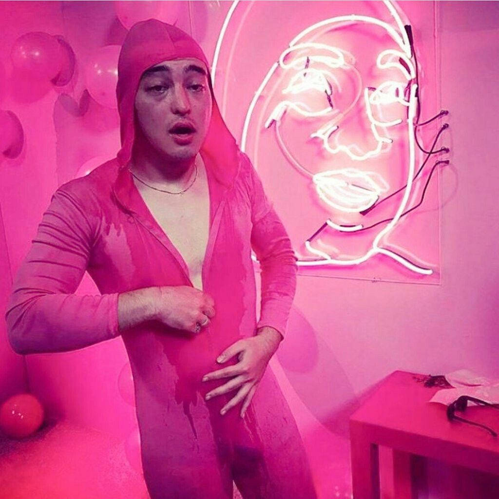filthy frank 桌布 壁紙 — 一個穿著粉紅色連帽衫的人站在一個霓虹粉紅色的房間裡，身後有一件發光的臉部藝術品。