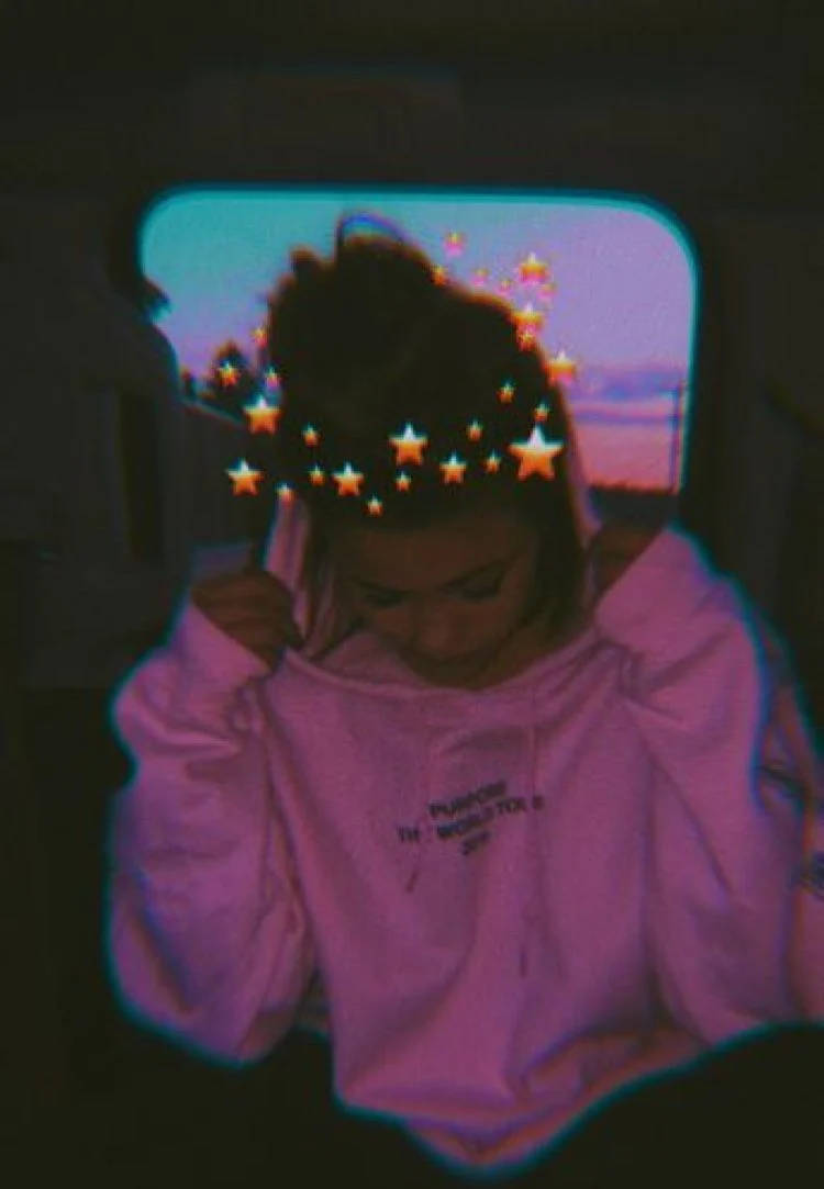 女孩 桌布 壁紙 — 一個穿著粉紅色連帽衫的人黃昏時坐在車內，頭上有數位疊加的發光星星。