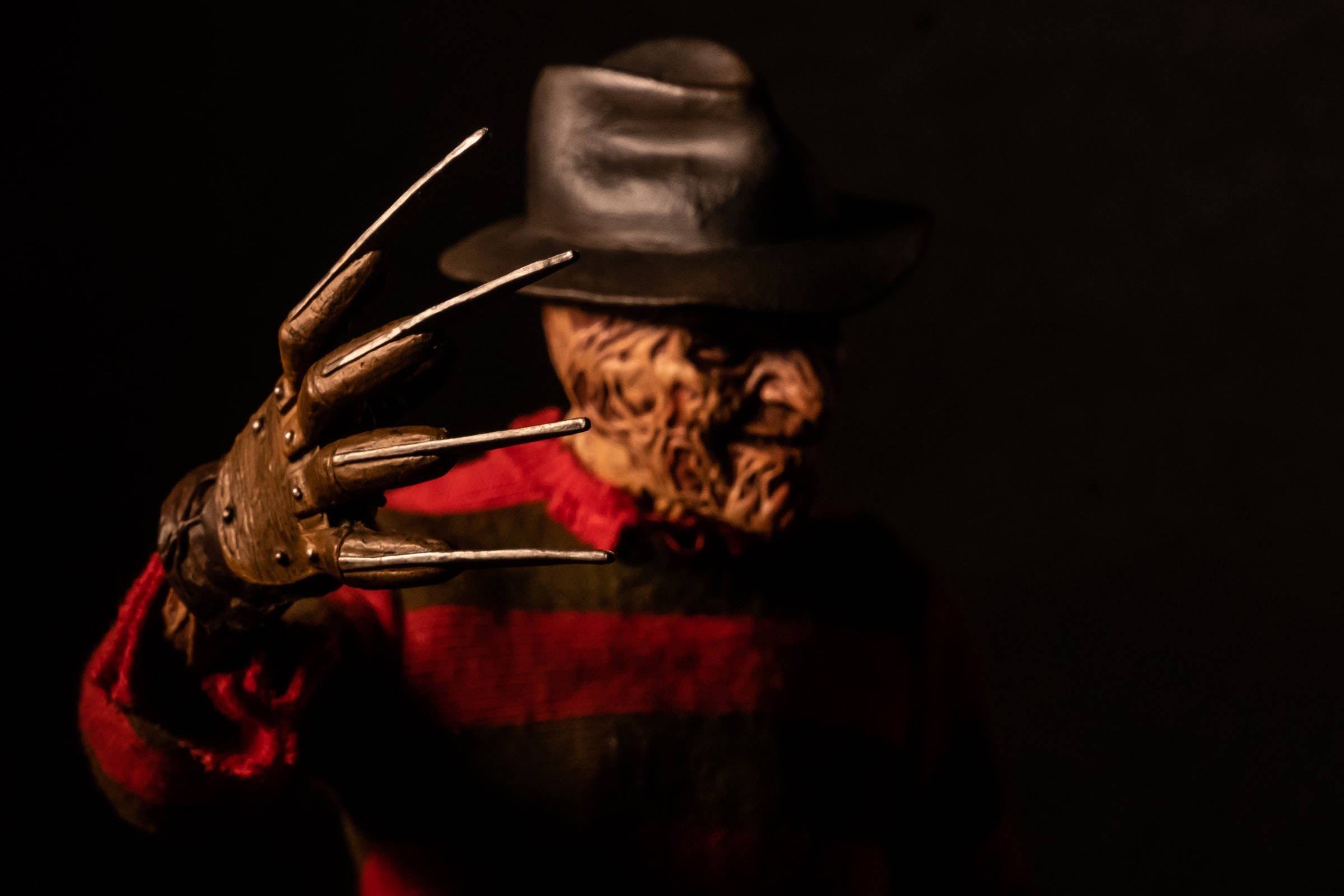 Freddy 桌布 壁紙 — 一個穿著紅白條紋衫和帽子的恐怖佛萊迪·克魯格，在黑暗背景下伸出他的利刃手套。