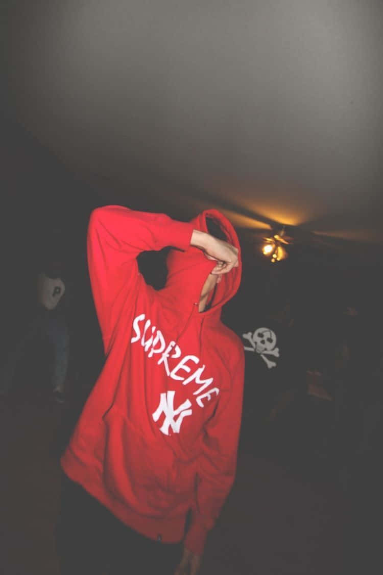 supreme 桌布 壁紙 — 一個穿著紅色Supreme連帽衫的人，在一個光線昏暗、有溫暖頂燈的房間裡把帽子拉過頭頂。