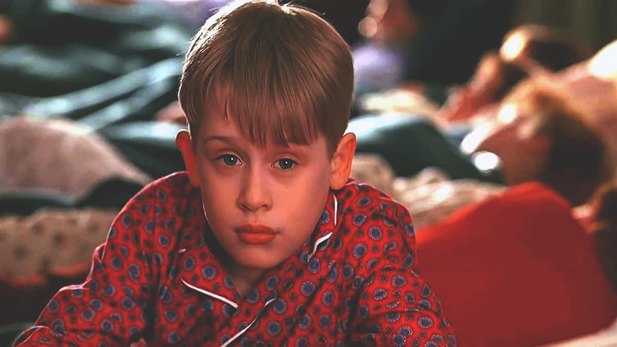 Home Alone 桌布 壁紙 — 一個穿著紅色圖案睡衣的小男孩在柔和光線的臥室裡專注地凝視著相機。
