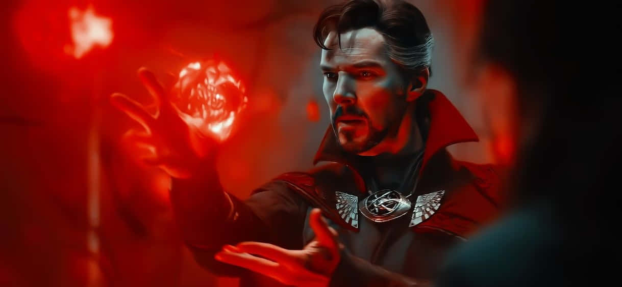 Doctor Strange 2 桌布 壁紙 — 一個穿著紅色斗篷的男人在黑暗神秘的環境中通過雙手引導發光的紅色能量。
