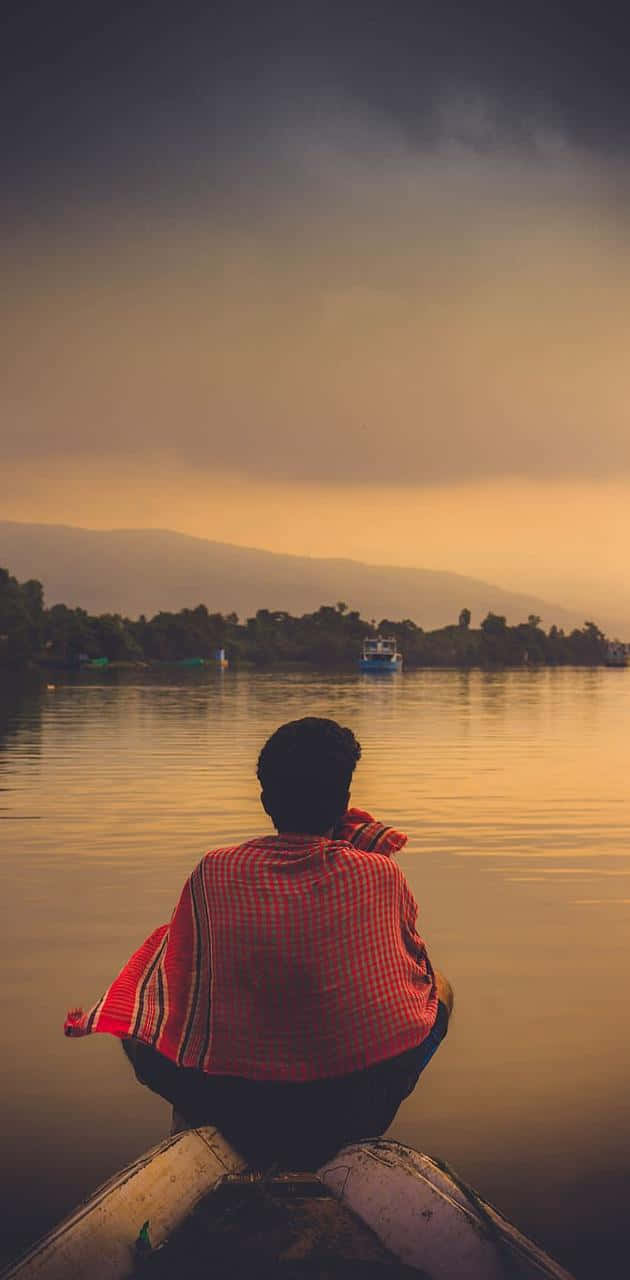 Lake 桌布 壁紙 — 一個穿著紅色格子襯衫的人坐在船上，在日落時分凝視遠處的山脈和平靜水面上的小船。