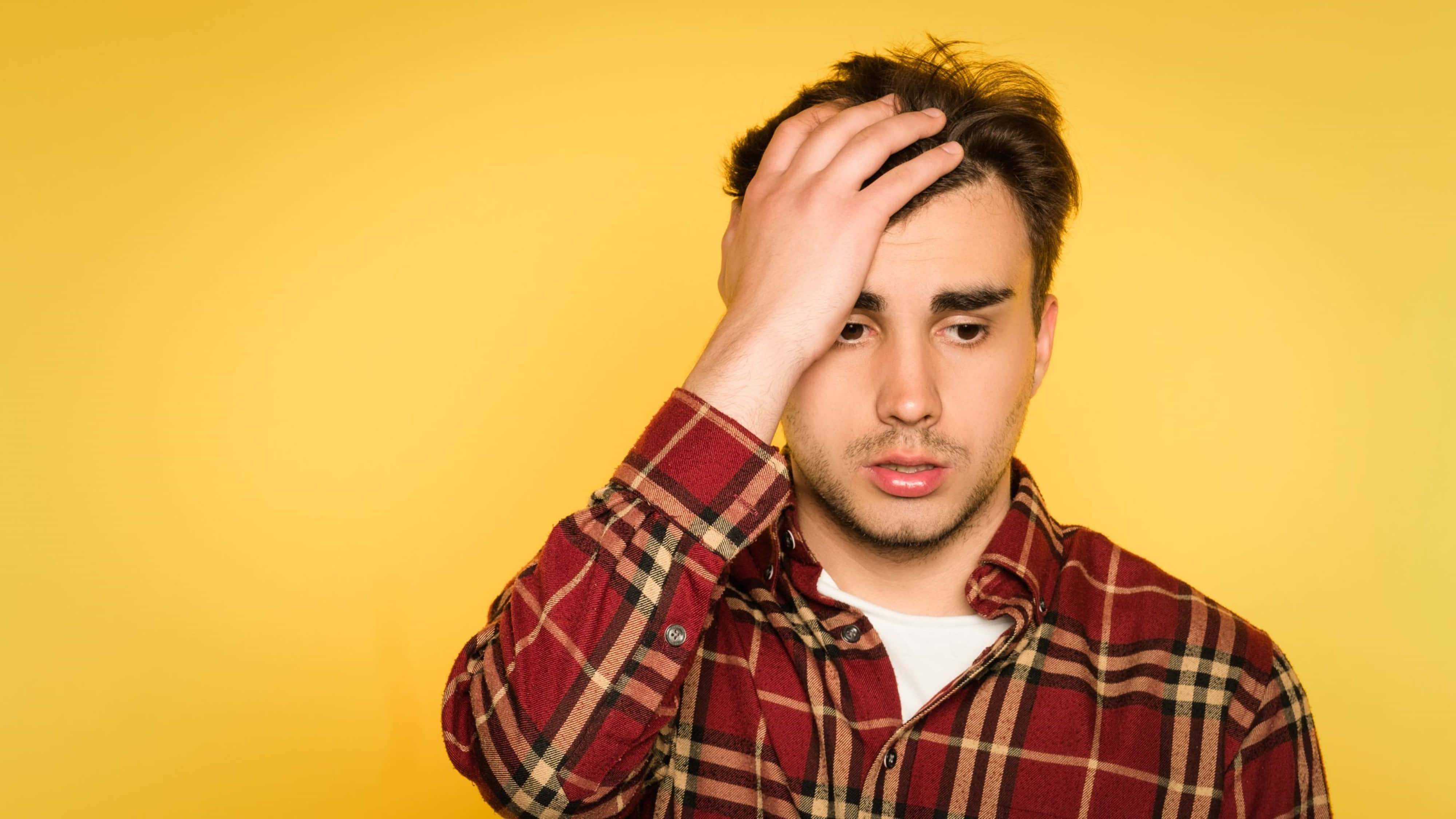 boys attitude 桌布 壁紙 — 一個穿著紅色格子襯衫的年輕男子，在純黃色背景前沮喪地抱著頭。