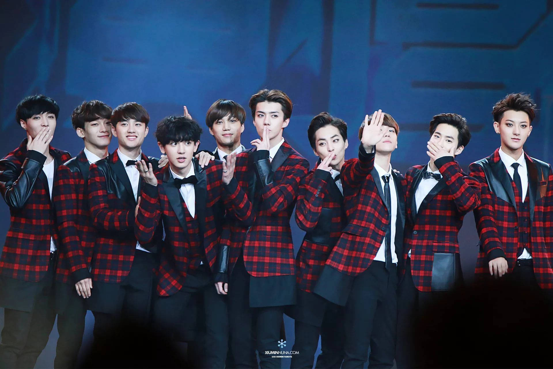 K-pop 桌布 壁紙 — 一個穿著紅色格紋外套的K-pop團體在藍色燈光昏暗的舞台上俏皮地擺姿勢。