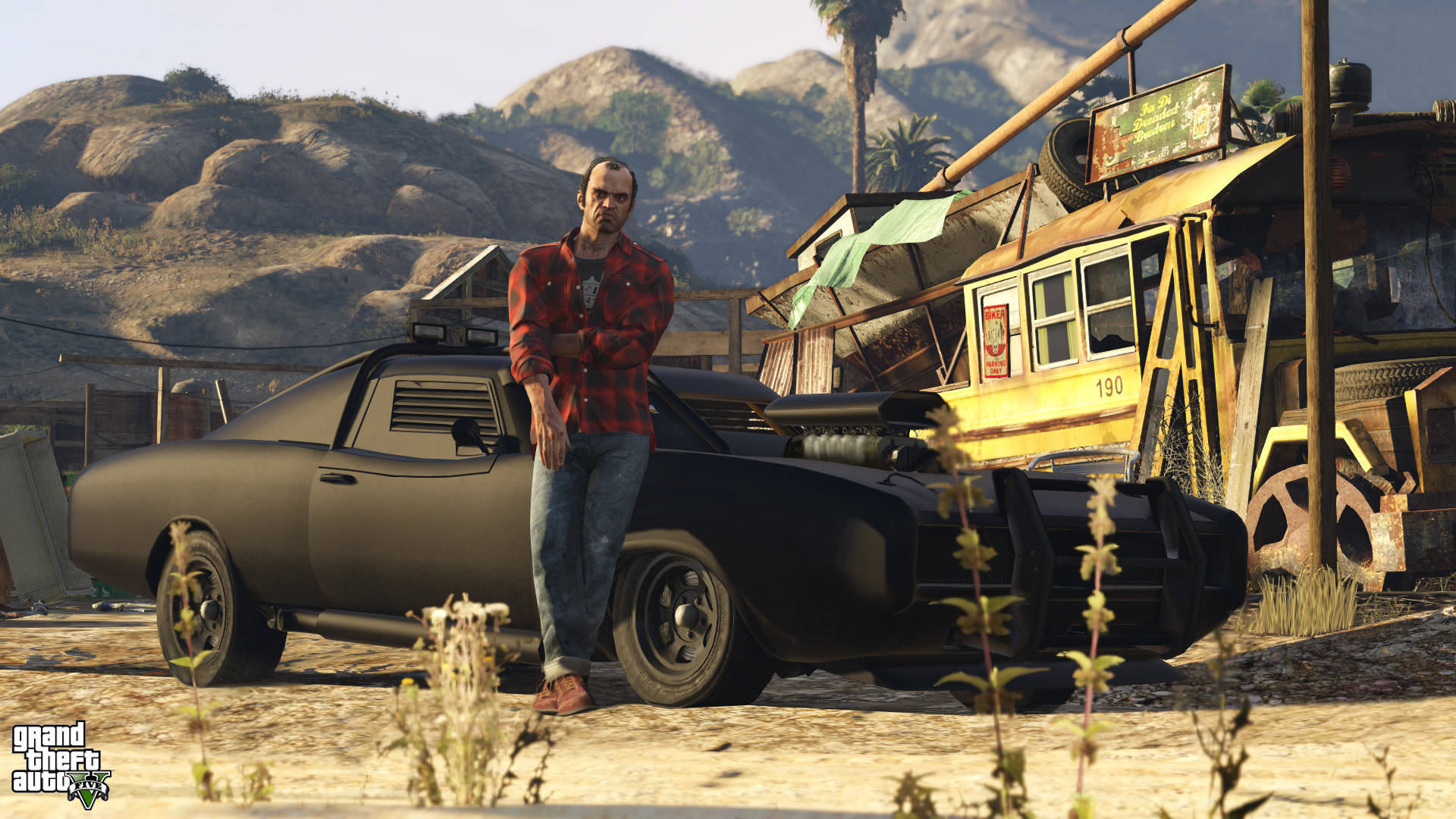 Gta 桌布 壁紙 — 一個穿著紅色格紋襯衫的男人在一個塵土飛揚的沙漠廢車場裡，靠著一輛黑色肌肉車，背景有山。