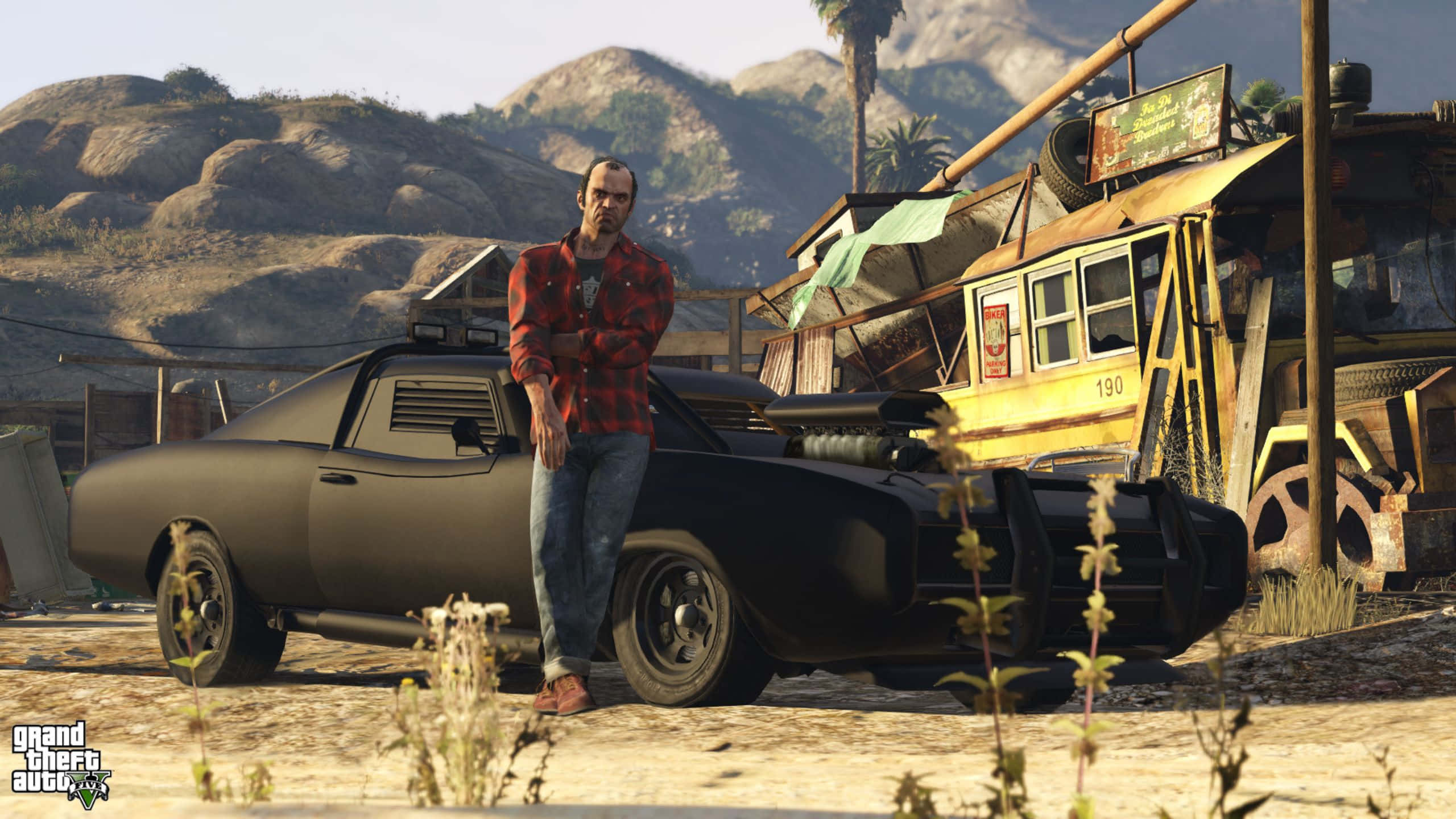 Grand Theft Auto V 桌布 壁紙 — 一個穿著紅色格紋襯衫的男人靠在一輛黑色肌肉車上，背景是塵土飛揚的沙漠廢車場和山脈。