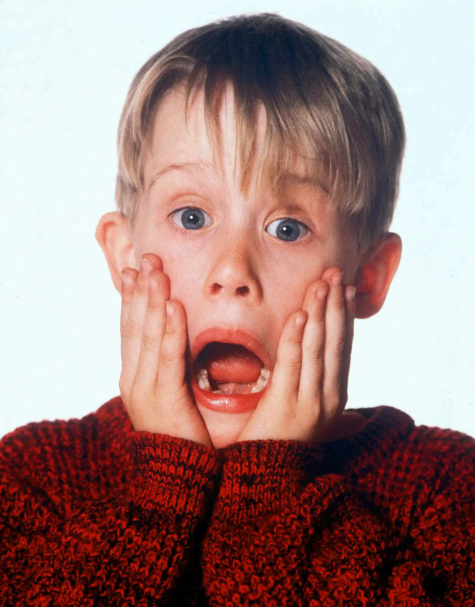 Home Alone 桌布 壁紙 — 一個穿著紅色毛衣的小男孩，睜大眼睛，張開嘴巴，雙手按著臉頰，在純白色背景前凝視。