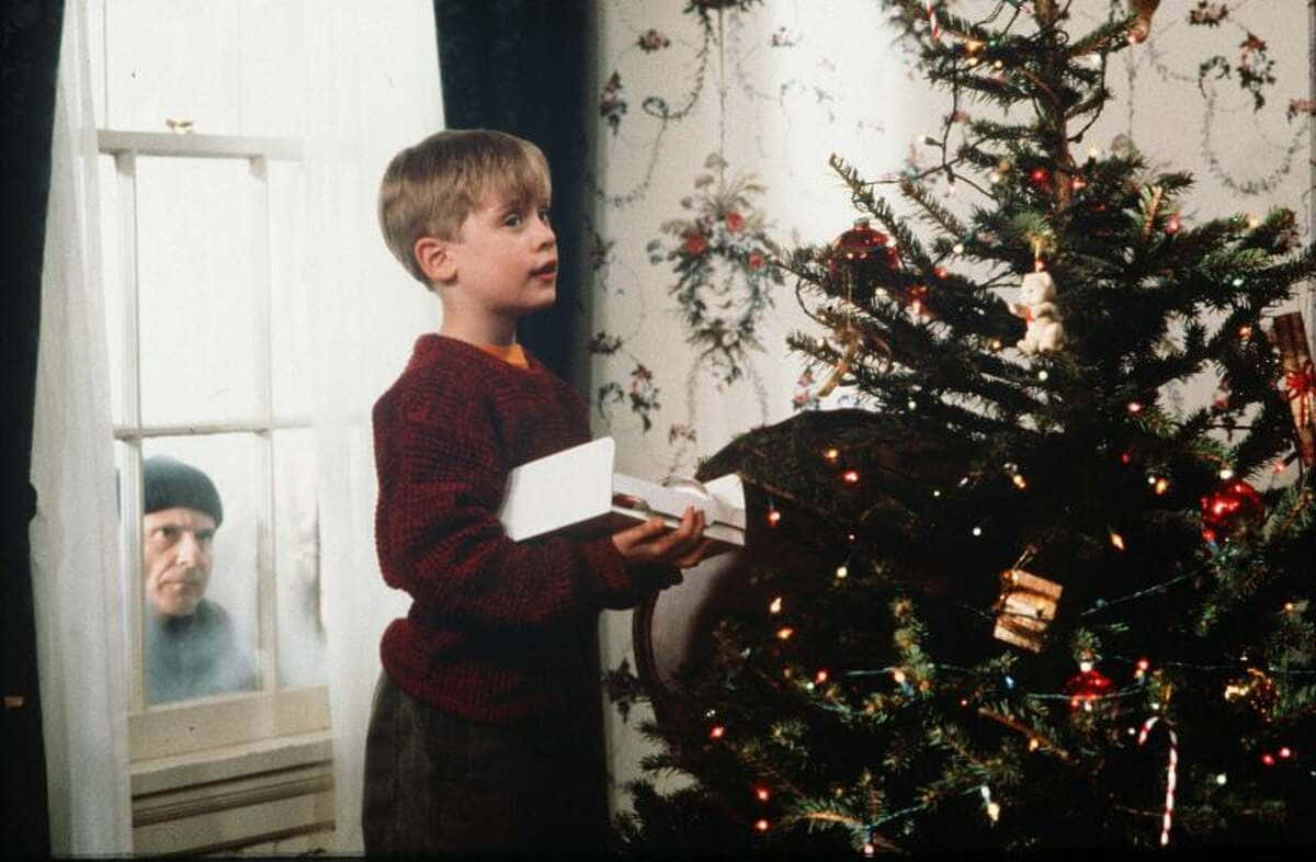 Home Alone 桌布 壁紙 — 一個穿著紅色毛衣的小男孩在裝飾好的聖誕樹旁拿著禮物，一個男人從附近的窗戶窺視。