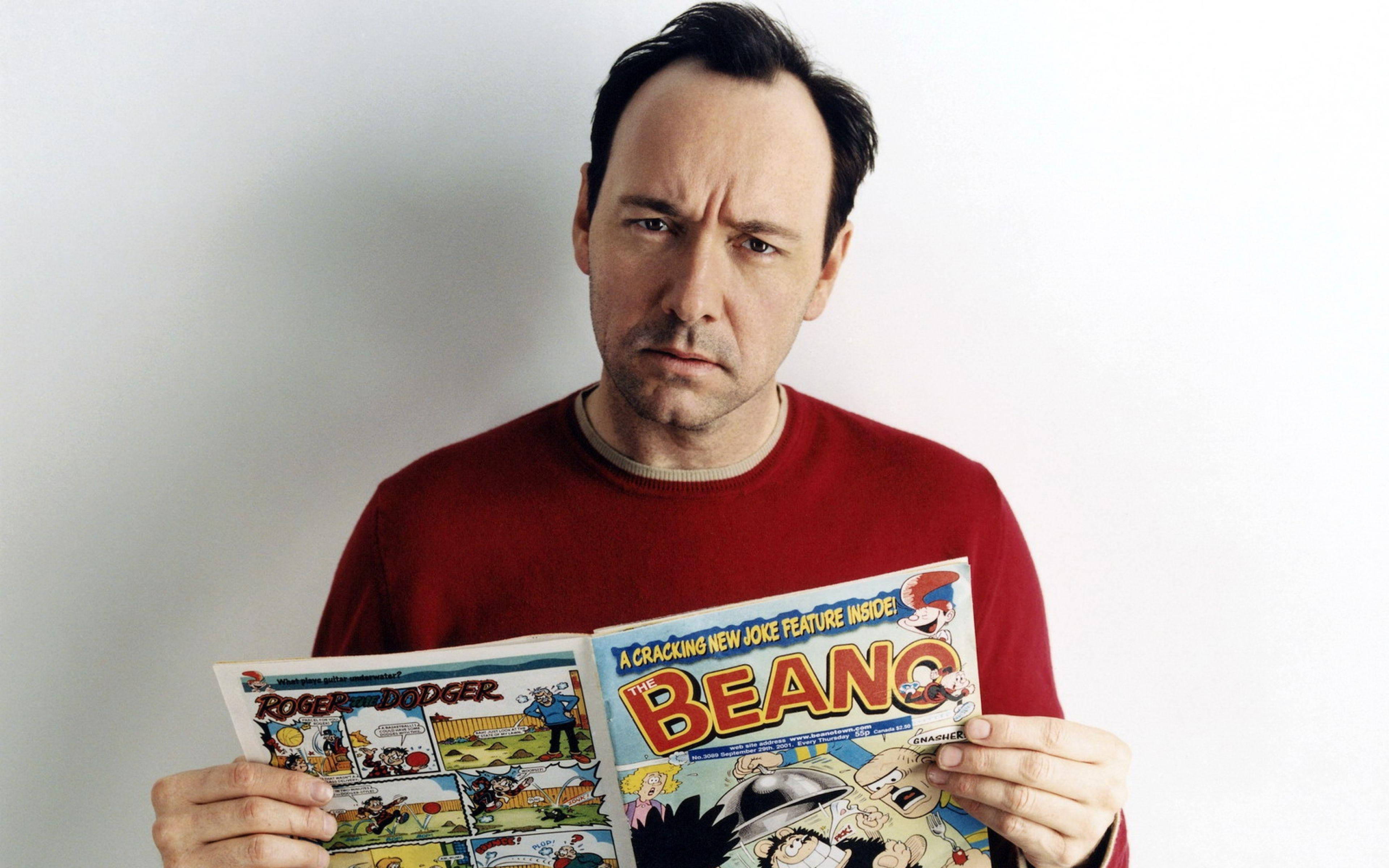 Comics 桌布 壁紙 — 一個穿著紅色毛衣的男人，拿著一本復古Beano漫畫書，對著白色牆壁打開。