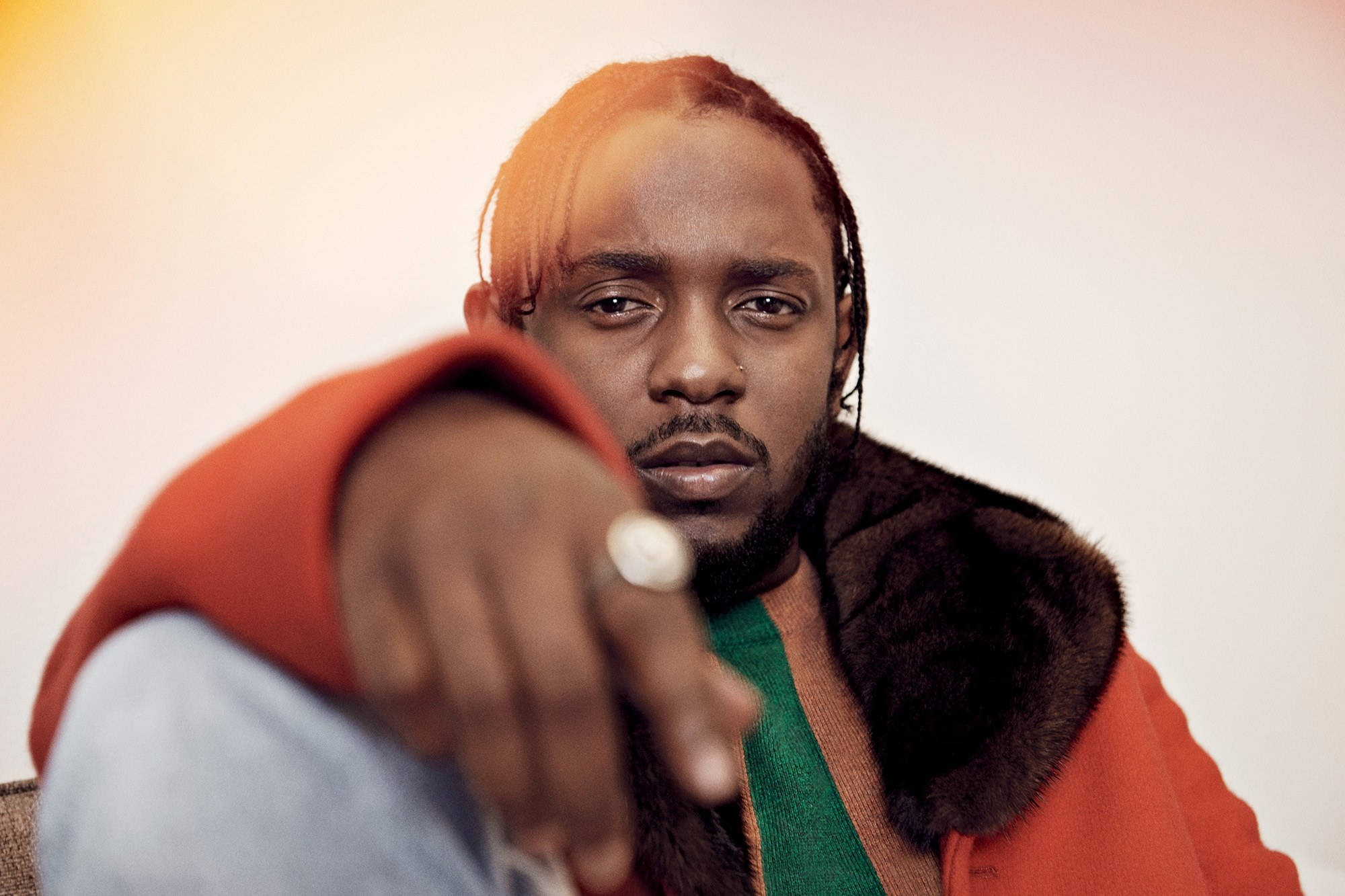 Kendrick 桌布 壁紙 — 一個穿著紅色毛領大衣的男人，在溫暖的燈光下，表情嚴肅地直接指向鏡頭。