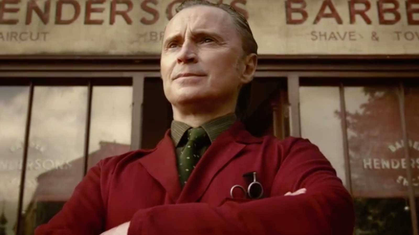 actor 桌布 壁紙 — 一個穿著紅色理髮外套的男人自信地交叉雙臂站在一個復古理髮店招牌前。