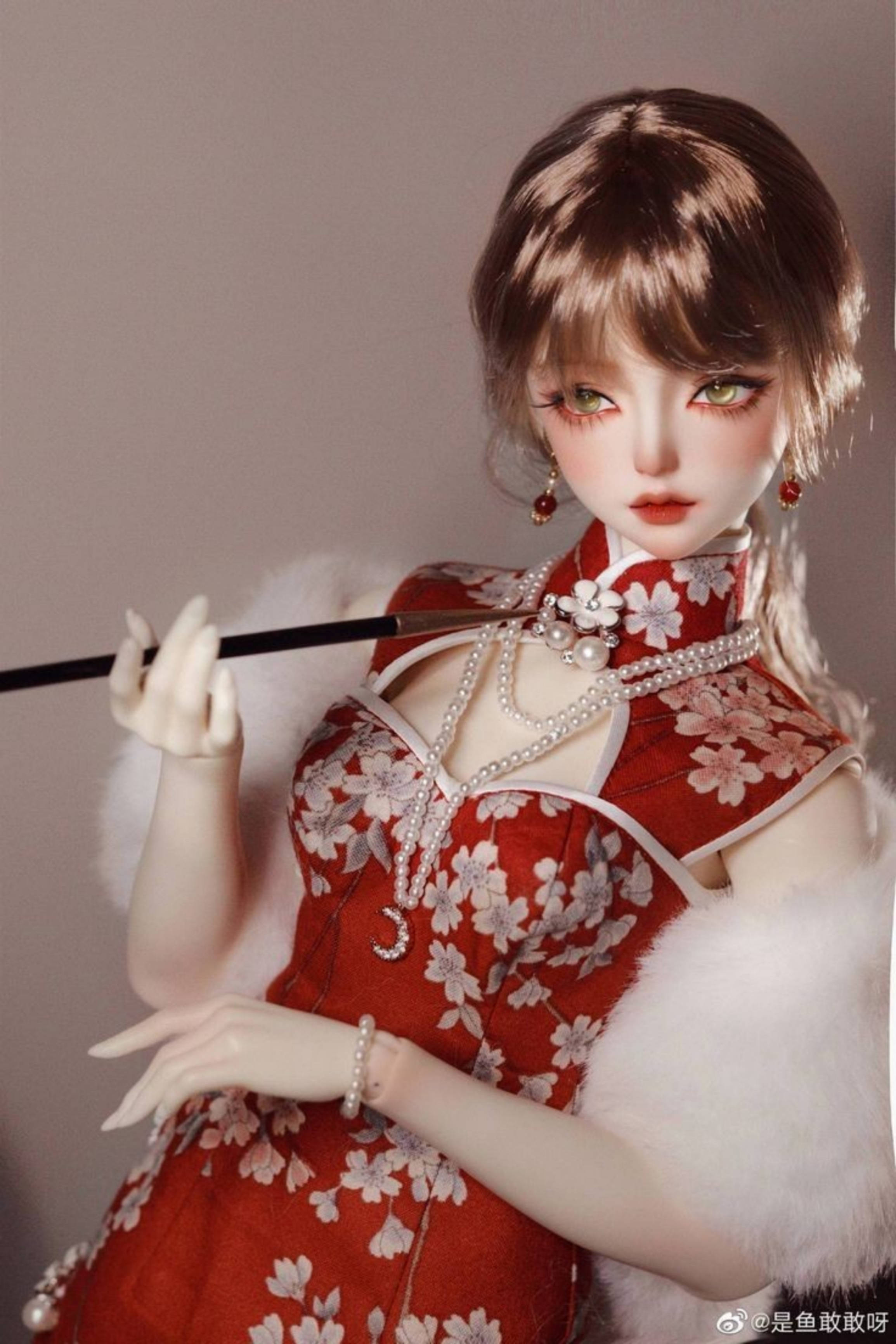 Doll 桌布 壁紙 — 一個穿著紅色花卉旗袍、帶白色毛邊的玩偶，在柔和的米色背景前拿著一個黑色煙嘴。