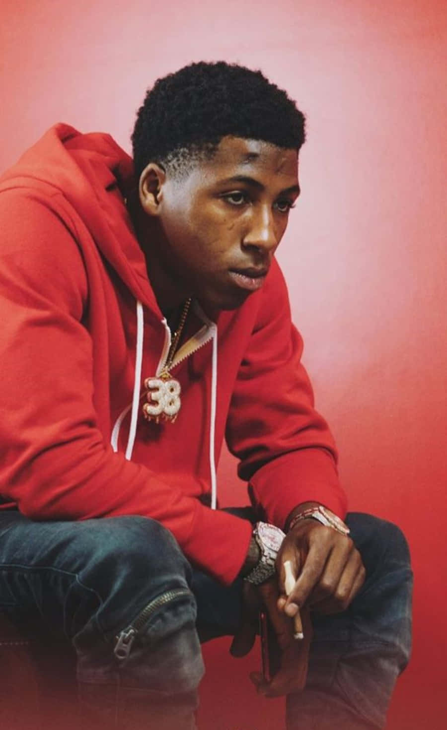 NBA YoungBoy 桌布 壁紙 — 一個穿著紅色連帽衫和牛仔褲的年輕男子坐在純紅色背景前，手持香菸，表情嚴肅。