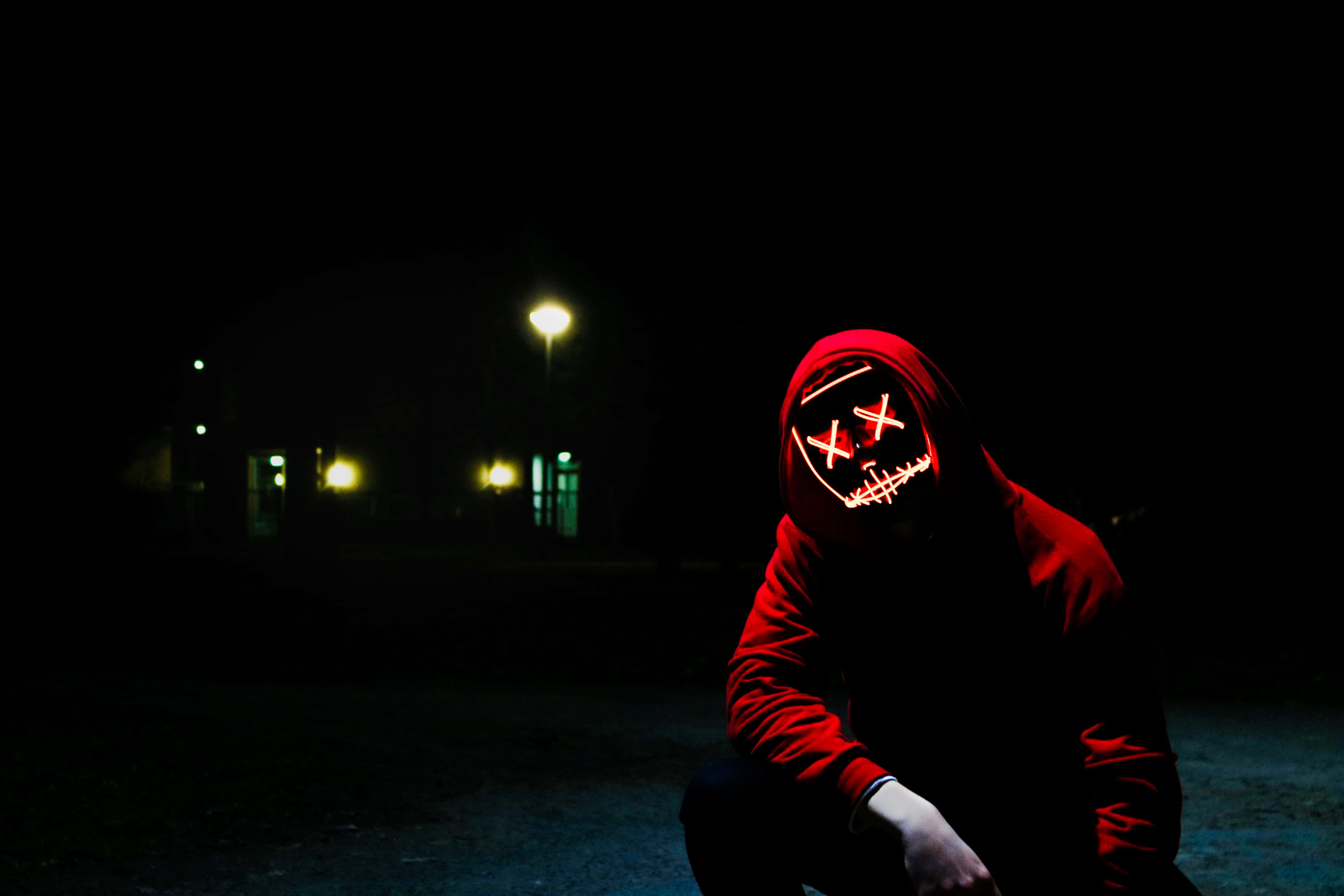 Unsettling 桌布 壁紙 — 一個穿著紅色連帽衫的人夜晚蹲著，戴著發光的紅色LED面具，面具上有X形眼睛和縫合的嘴巴。