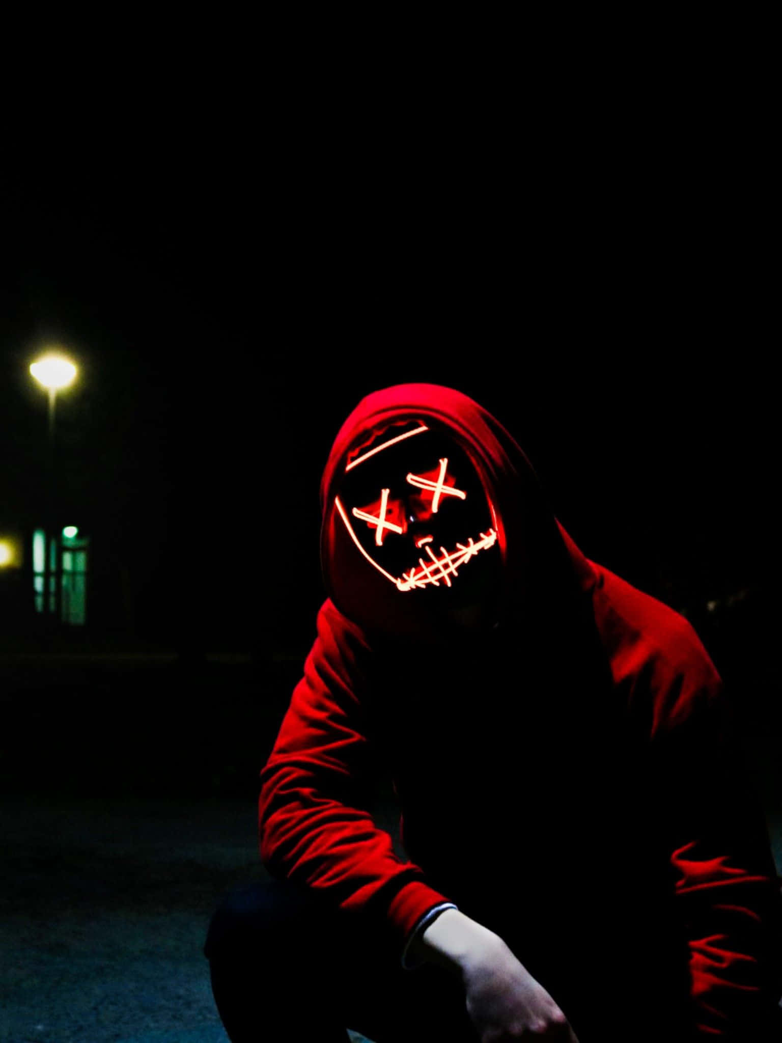 Red Hoodie 桌布 壁紙 — 一個穿著紅色連帽衫的人夜晚蹲著，戴著發光的紅色LED面具，面具上有縫合的X形眼睛和嘴巴。