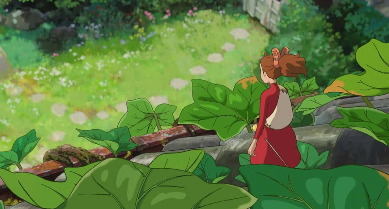 The Secret World Of Arrietty 桌布 壁紙 — 一個穿著紅色連衣裙的小女孩站在巨大的綠色葉子中，俯瞰著一條陽光普照、點綴著白色花朵的花園小徑。