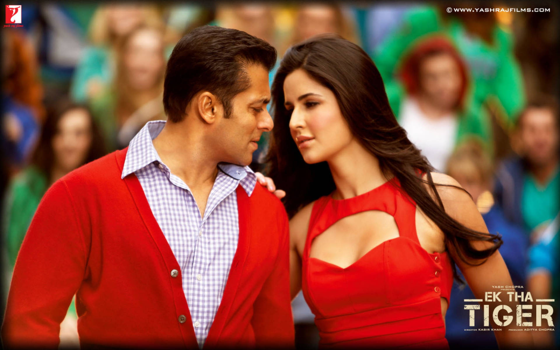 Salman Khan 桌布 壁紙 — 一個穿著紅色開襟衫的男人和一個穿著紅色連衣裙的女人在擁擠的體育場分享親密時刻。