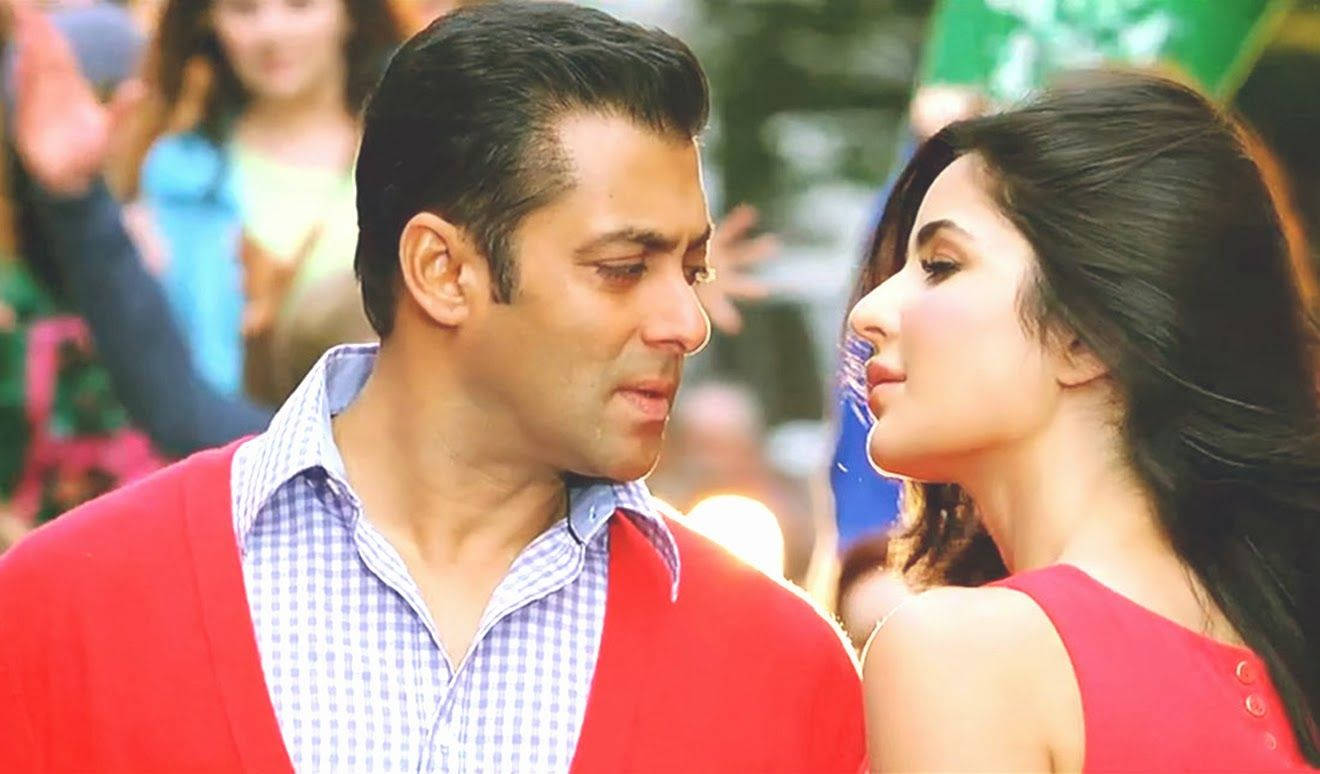 salman khan HD 桌布 壁紙 — 一個穿著紅色開襟衫的男人和一個穿著紅色連衣裙的女人在擁擠的戶外環境中互相凝視，分享親密時刻。