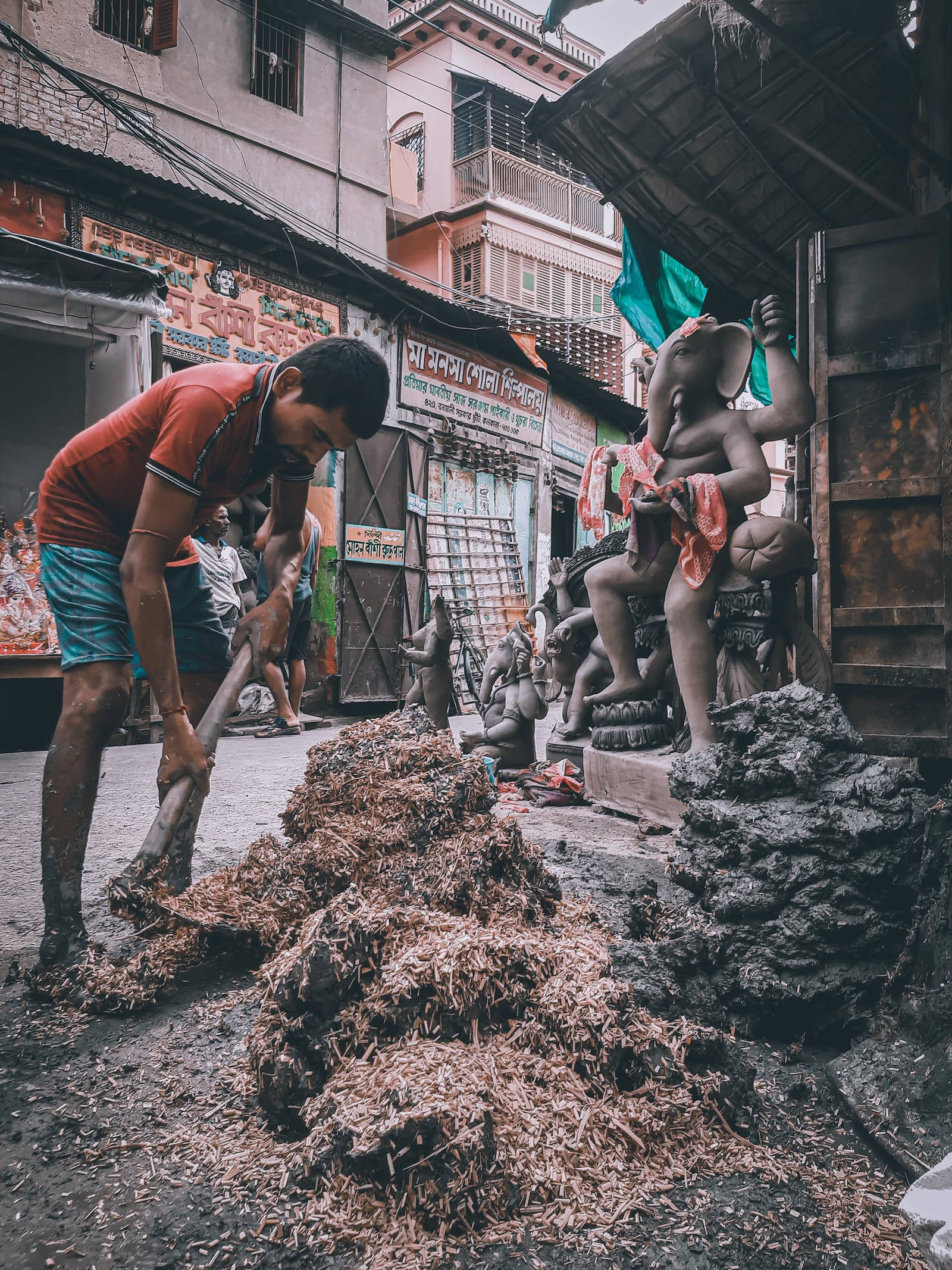 maa durga 桌布 壁紙 — 一個穿著紅衫的男人在繁忙的印度街市，在一個大型Ganesha雕像附近鏟木屑。
