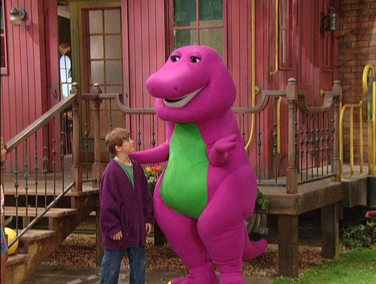 barney 桌布 壁紙 — 一個穿著紫色毛衣的小男孩站在一間有樓梯的紅色木屋外，旁邊是巨大的紫色恐龍巴尼。