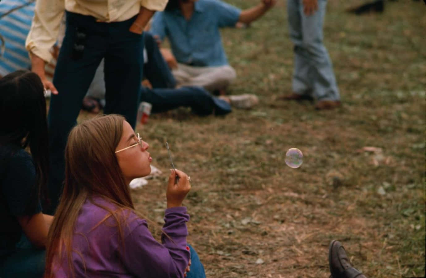 woodstock 桌布 壁紙 — 一個穿著紫色襯衫的小女孩在草地上吹肥皂泡，而其他人則在她周圍放鬆。