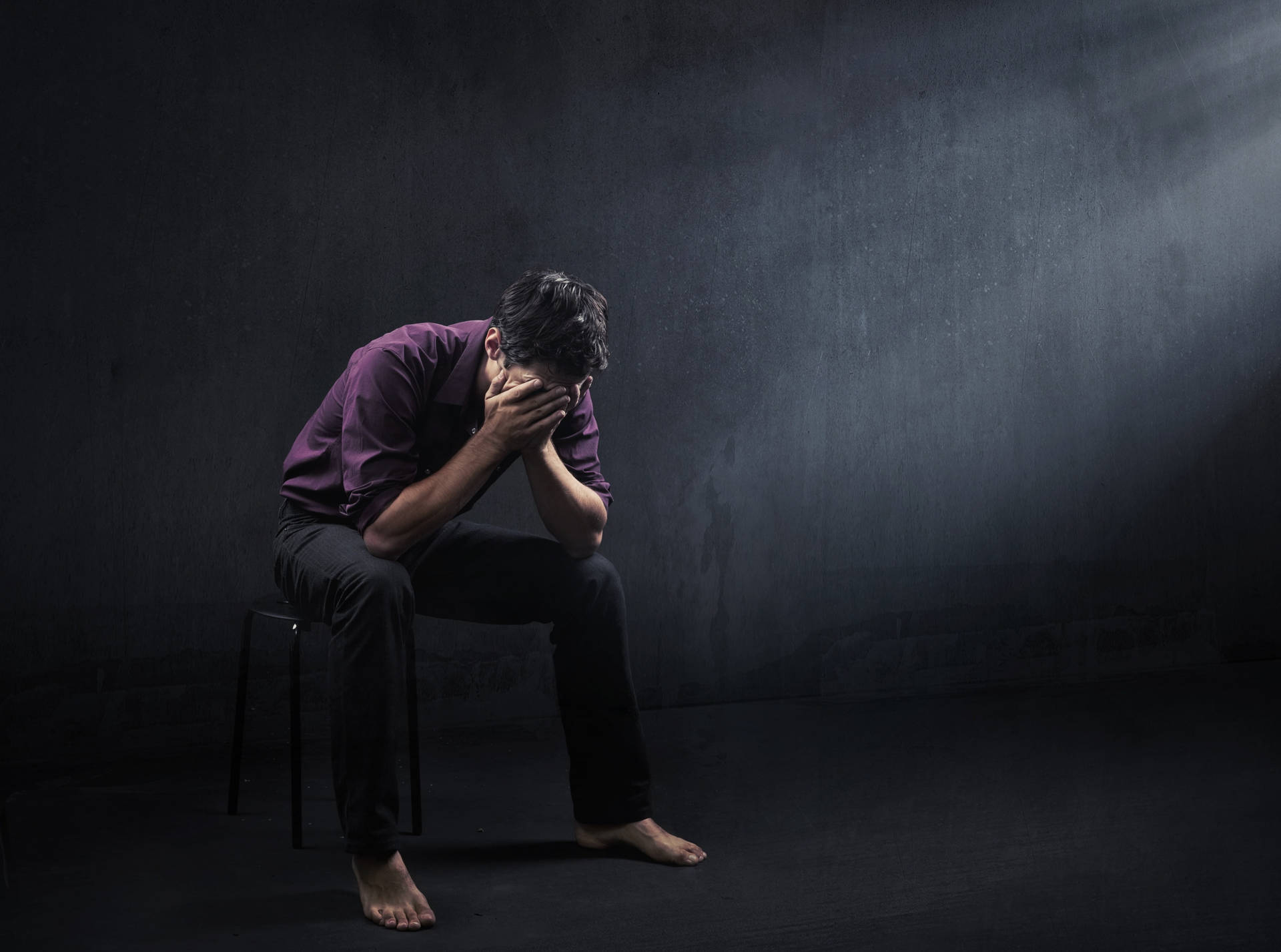 一個男人坐在凳子上，在黑暗的房間裡用聚光燈照射下掩面。 — 黑暗悲傷動圖 壁紙