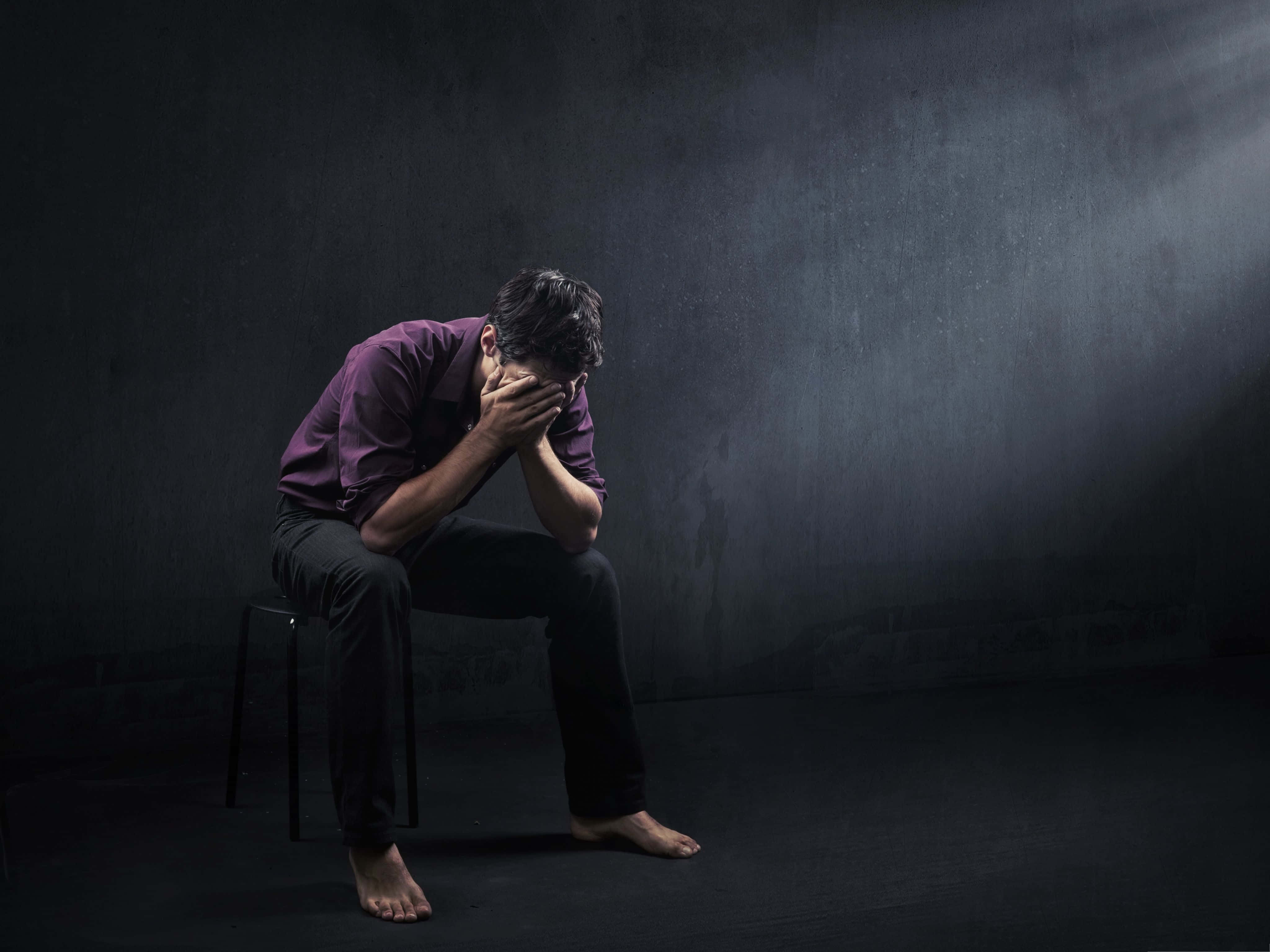 Depressing 桌布 壁紙 — 一個穿著紫色襯衫的男人獨自坐在昏暗房間的凳子上，絕望地用雙手摀住臉。