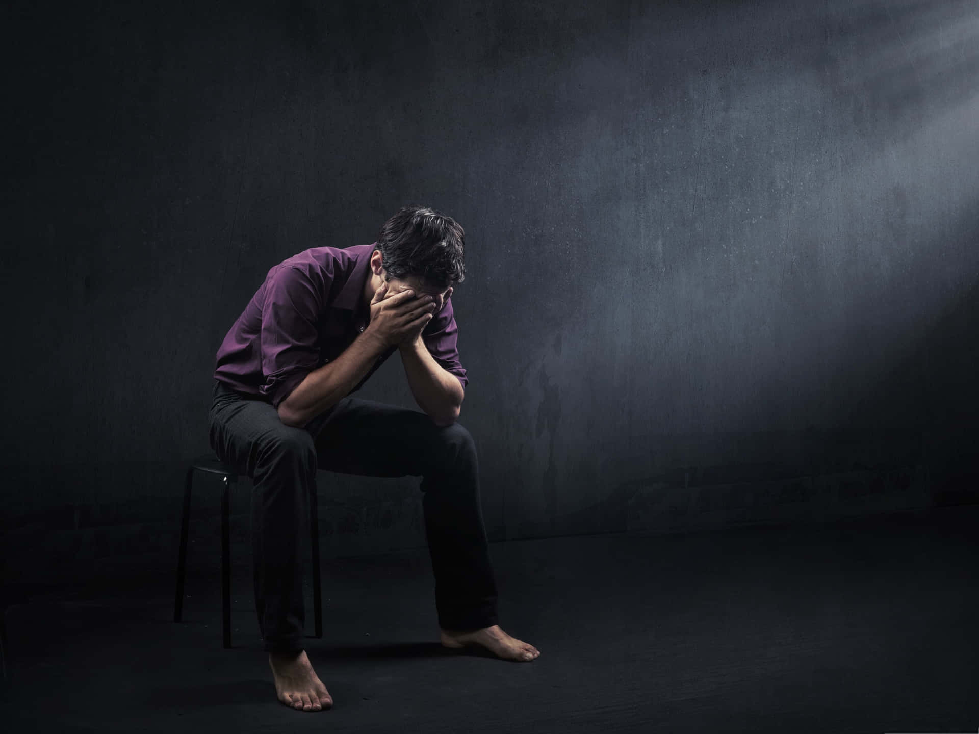 Alone 桌布 壁紙 — 一個穿著紫色襯衫的男人獨自坐在昏暗房間的凳子上，絕望地用雙手掩面。