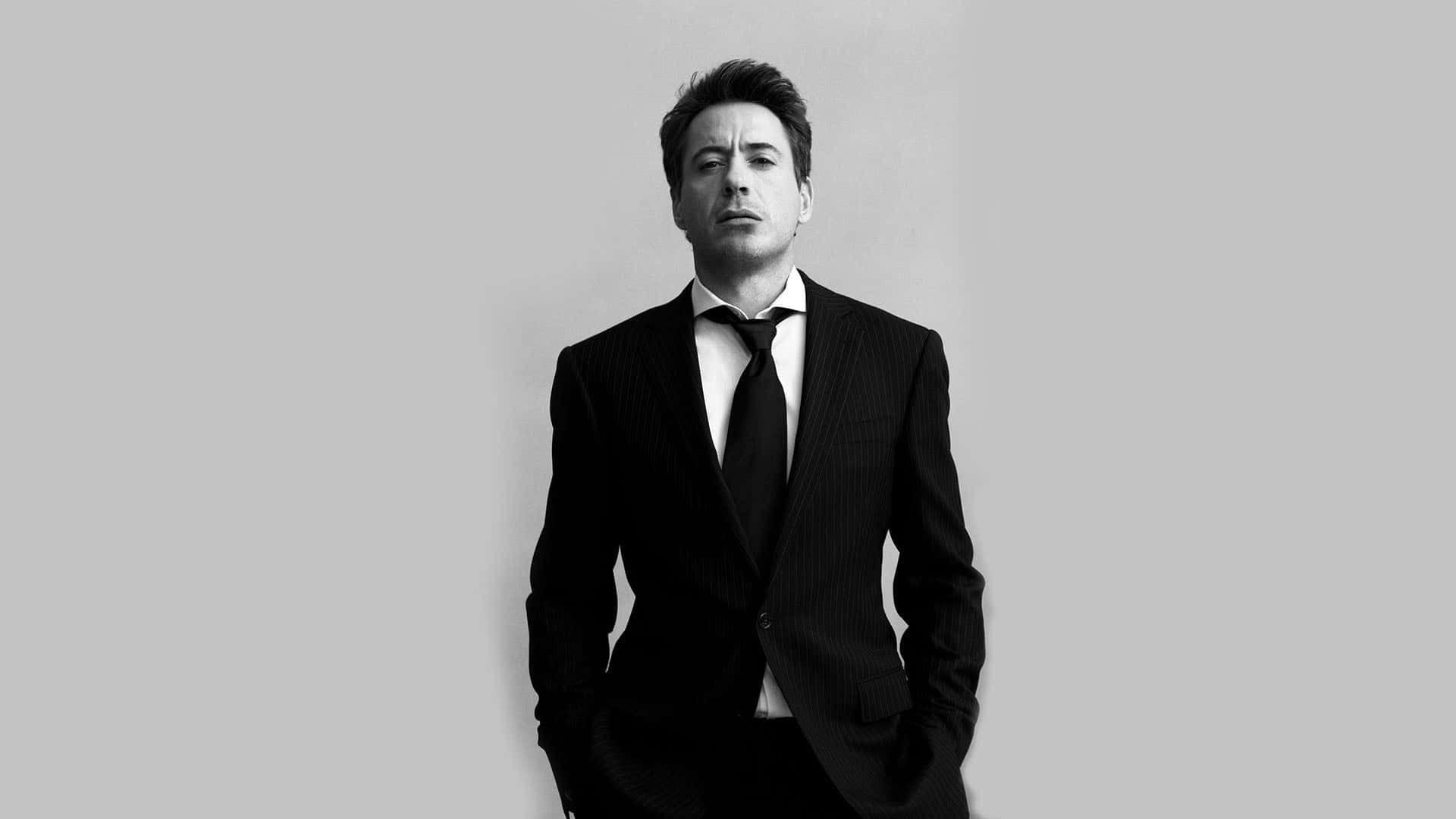 Man In Suit 桌布 壁紙 — 一個穿著細條紋西裝、雙手插袋的男人在純灰色背景前的黑白肖像。