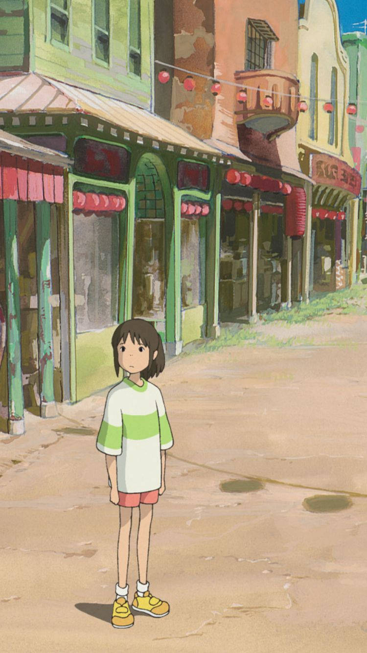 神隱少女 桌布 壁紙 — 一個穿著綠色和白色襯衫的小女孩獨自站在一條陽光普照的鵝卵石街道上，兩旁是色彩繽紛的復古商店和紅色燈籠。
