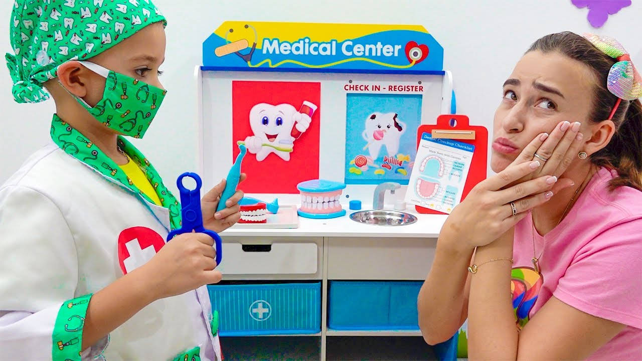Dentistry 桌布 壁紙 — 一個穿著綠色手術裝備的小孩在色彩繽紛的玩具牙科診所假裝治療一位女士的牙齒。