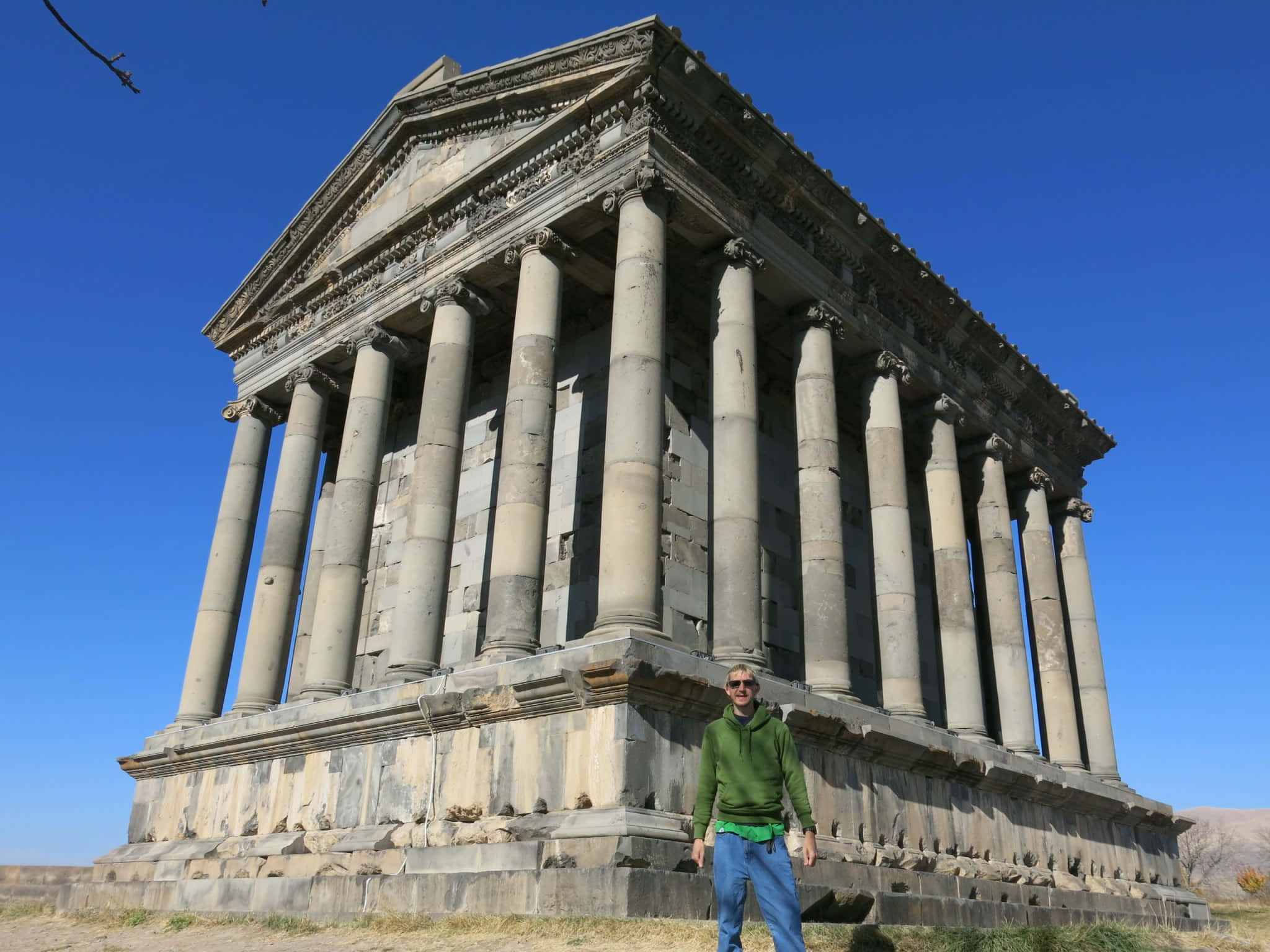 Building 桌布 壁紙 — 一個穿著綠色連帽衫的人站在宏偉廢墟寺廟的古老石柱前，背景是晴朗的藍天。