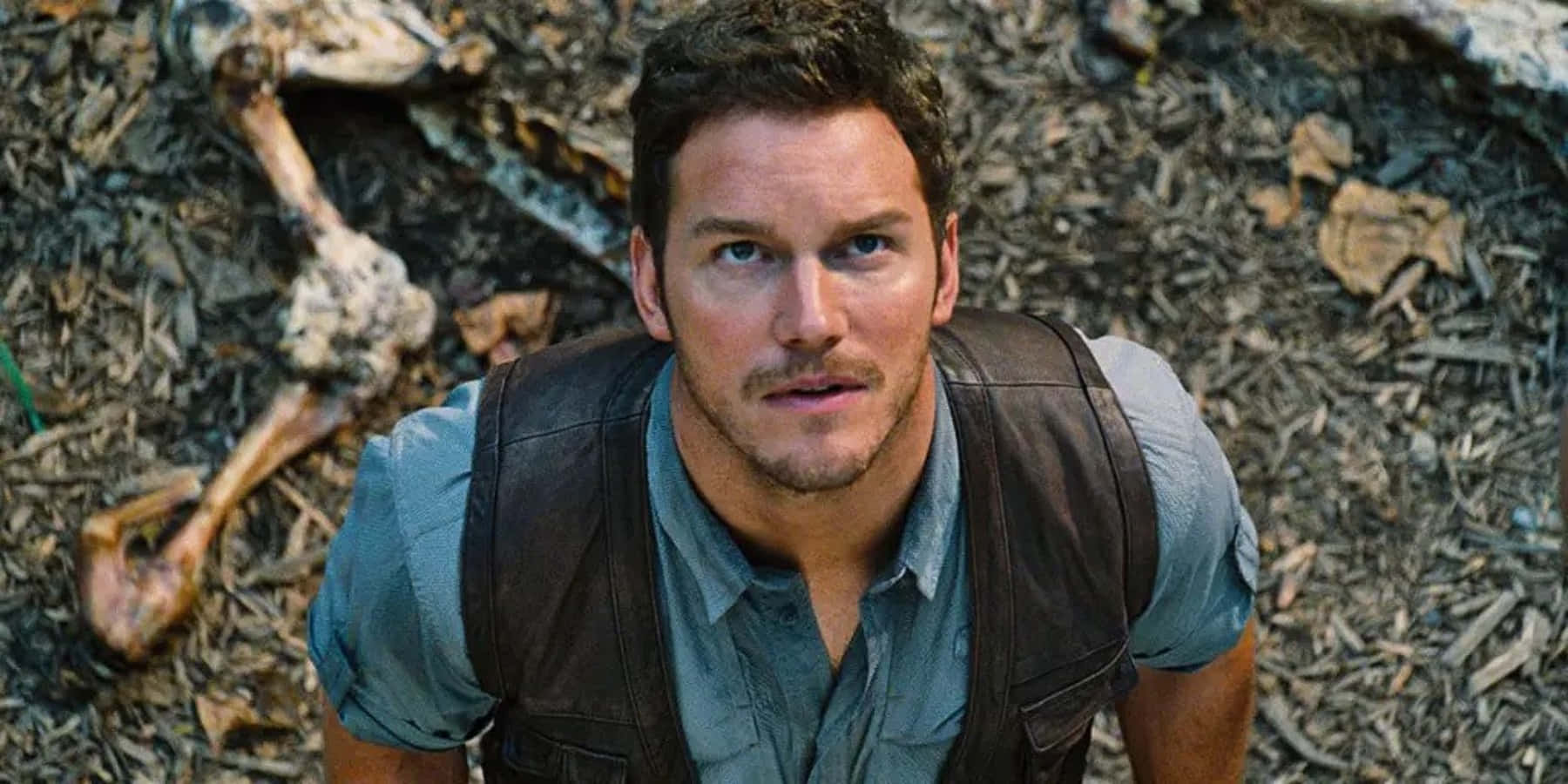 Jurassic World 桌布 壁紙 — 一個穿著背心的男人從佈滿動物骨頭的森林地面抬頭看。