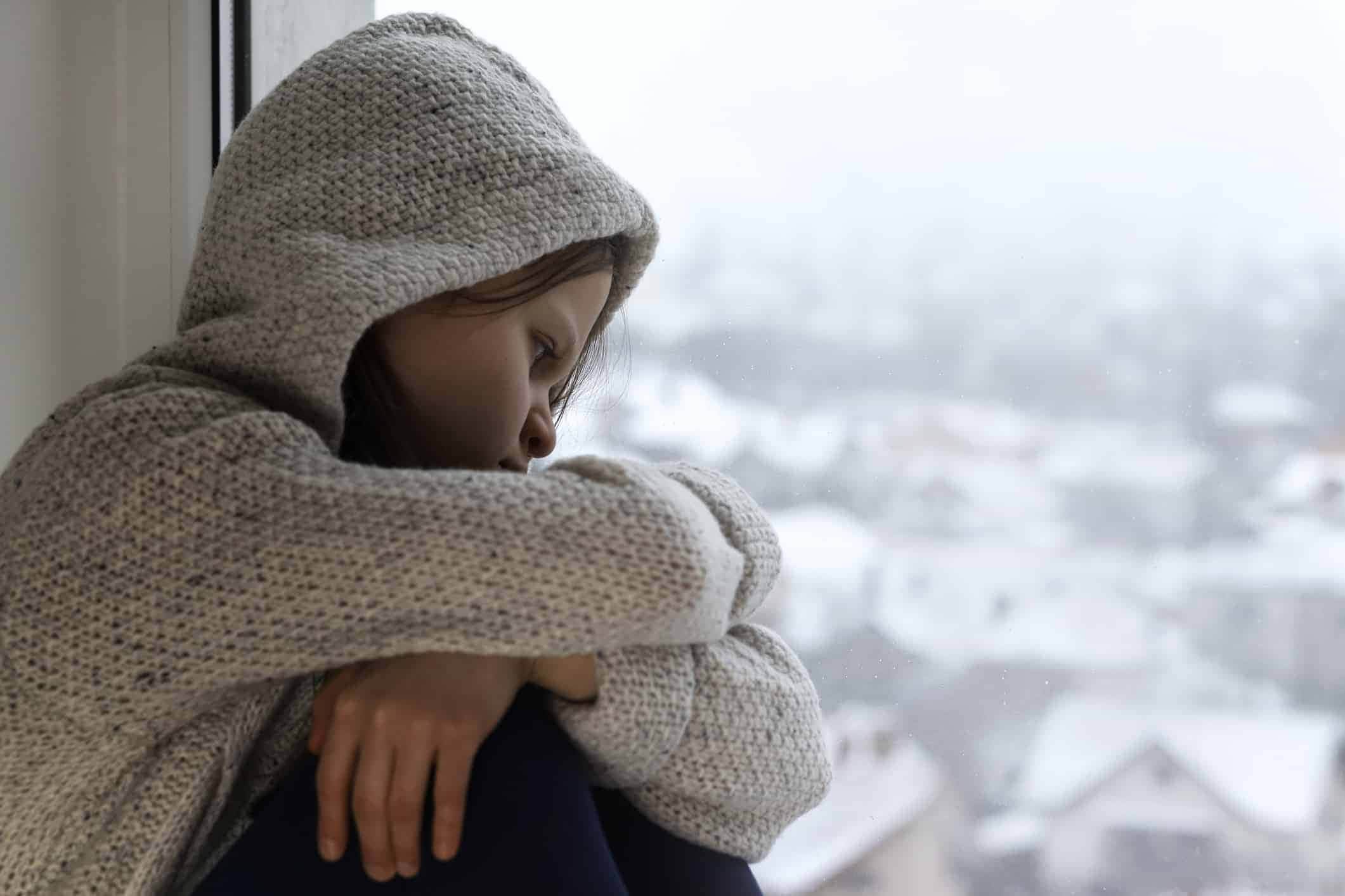 Depressed 桌布 壁紙 — 一個穿著舒適針織連帽衫的人坐在窗邊，眺望下方白雪覆蓋的小鎮。