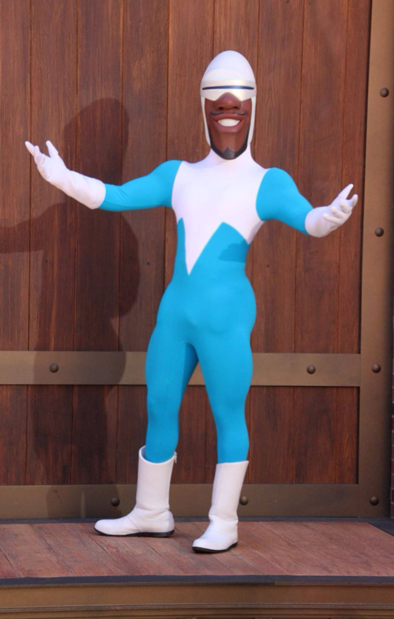 Frozone 桌布 壁紙 — 一個穿著藍白色超級英雄服裝的開朗人物，站在木門背景前，雙臂伸展。