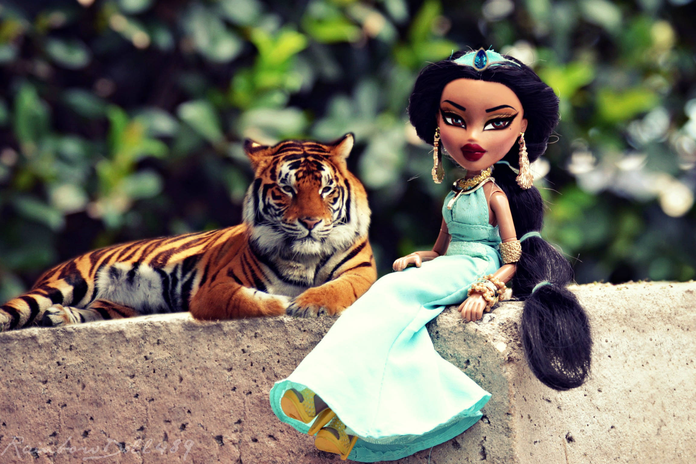 bratz 美學 桌布 壁紙 — 一個穿著藍綠色長袍的 Bratz 娃娃坐在石檯上，旁邊有一隻真老虎，背景是茂密的綠葉。