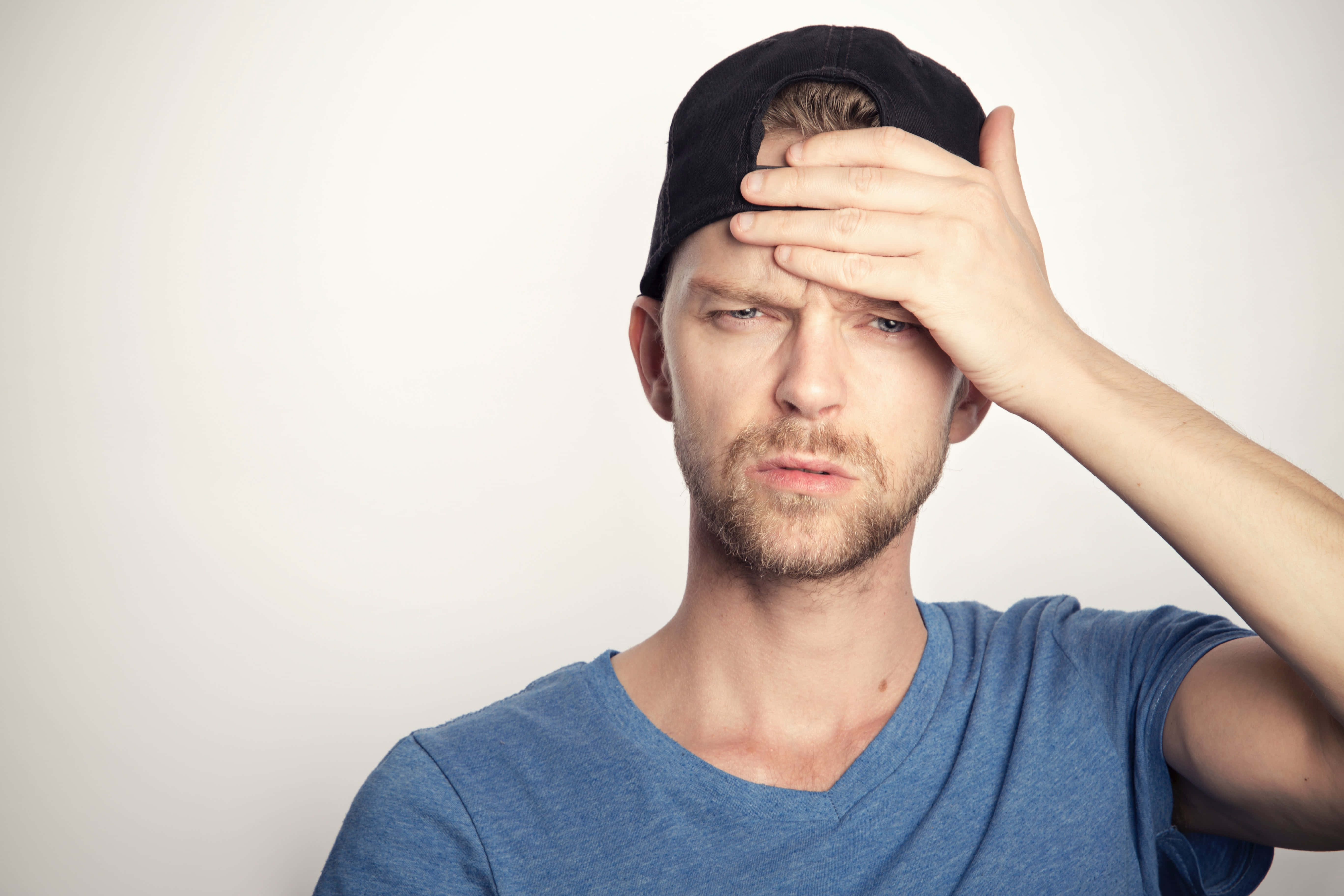Frustrated 桌布 壁紙 — 一個穿著藍色T恤和黑色帽子的男人，在純白色背景前用手遮擋眼睛。