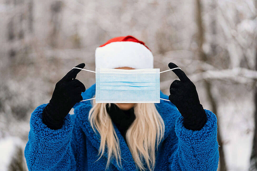 冬季桌面 桌布 壁紙 — 一個穿著藍色外套和聖誕帽的人，在雪白的冬季背景下，將醫用口罩遮在臉上。
